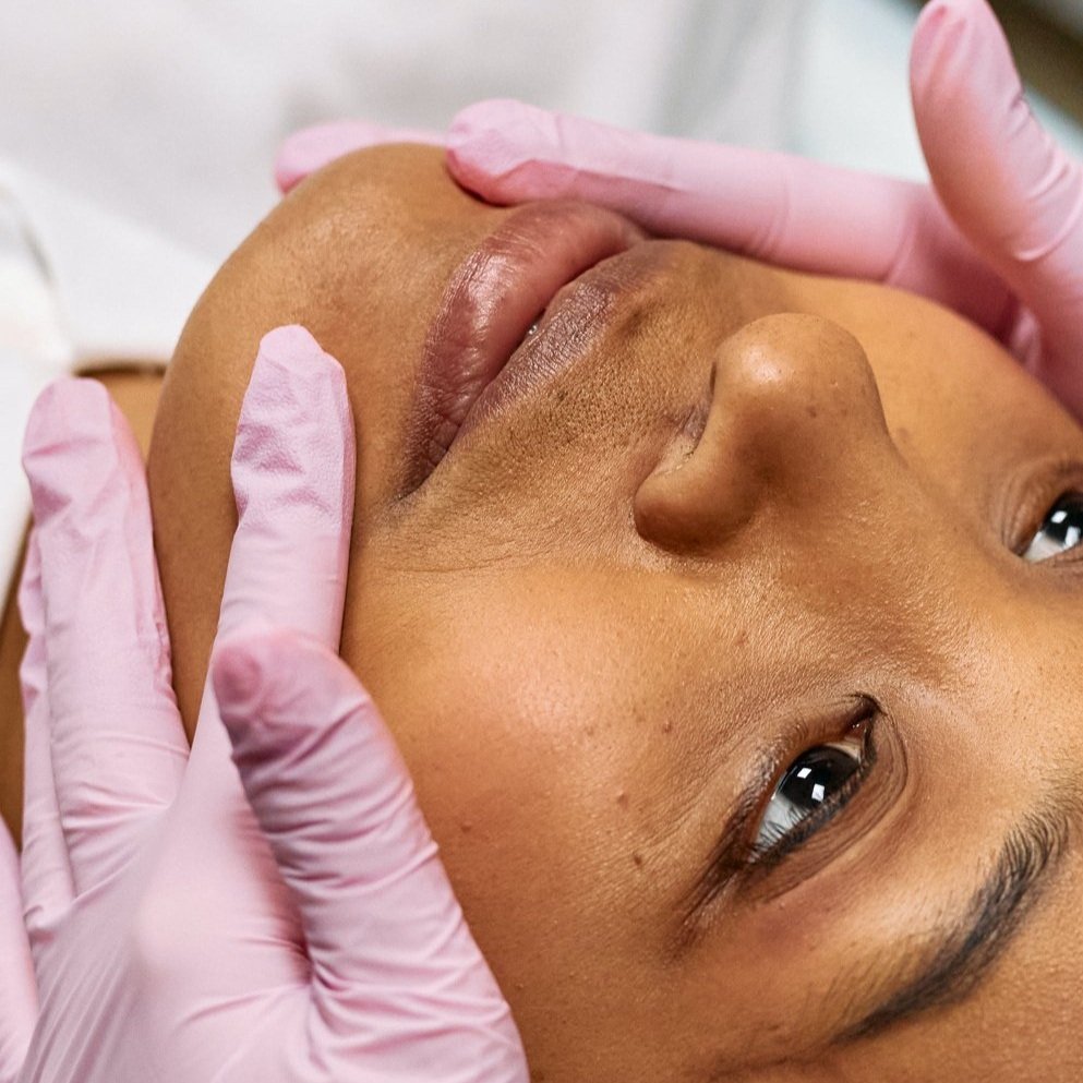 A person receiving a facial massage or treatment, with a healthcare professional wearing pink gloves gently pressing on their face.