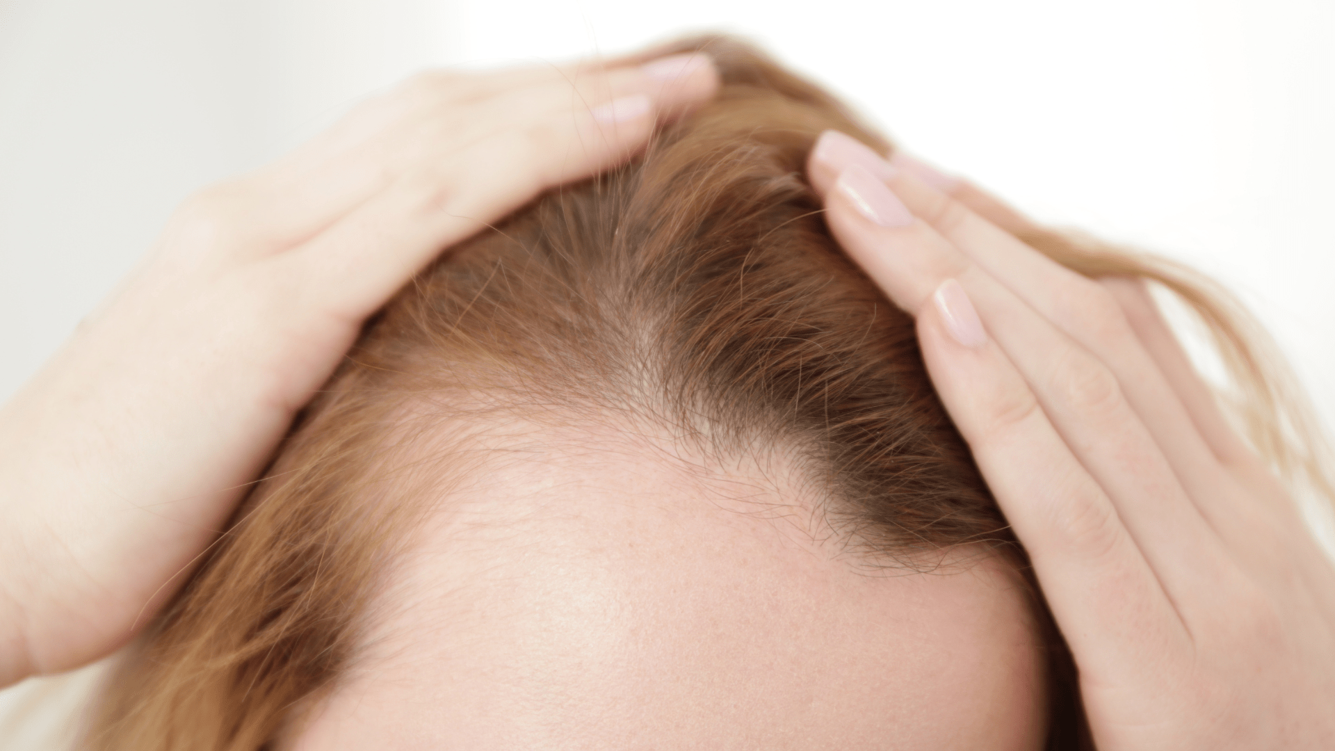 Close-up of a person with reddish-brown hair running their fingers through their scalp.