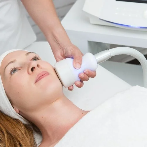 Woman receiving a facial treatment with a handheld device in a clinic or spa setting.