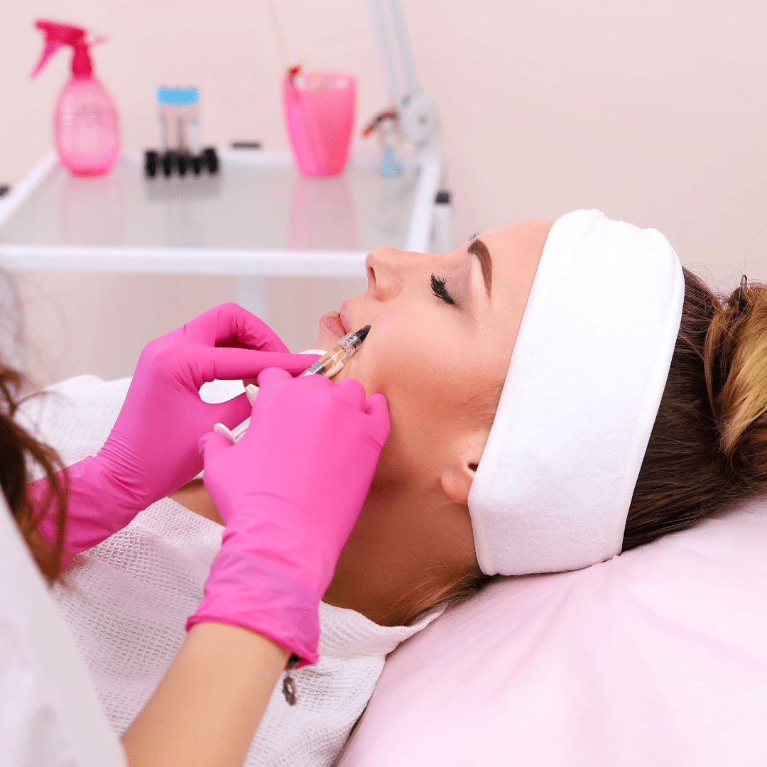 A woman receiving a cosmetic injection treatment while lying on a bed in a clinic, wearing a white headband and pink gloves.
