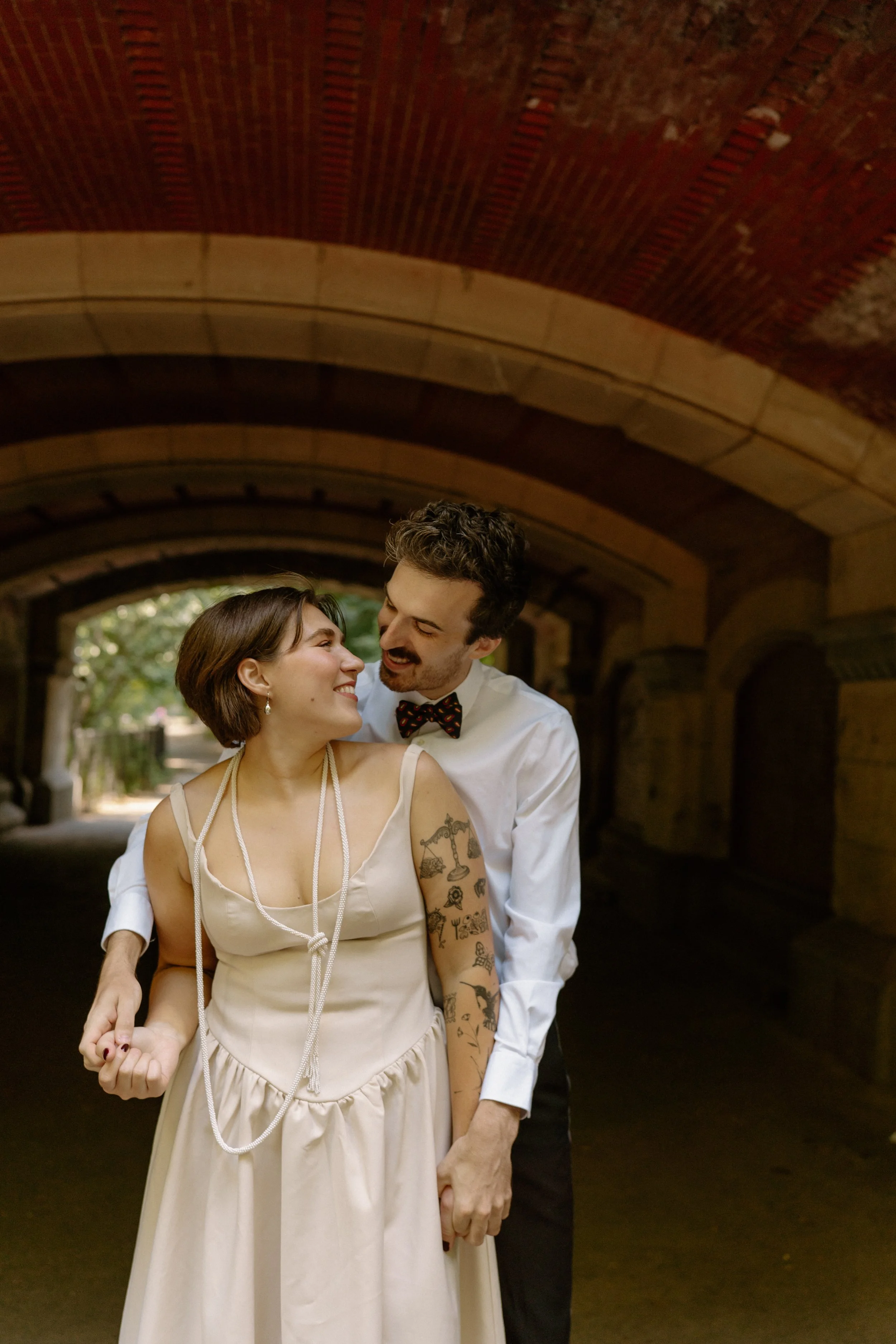 A happy couple embracing under a brick archway, smiling at each other.