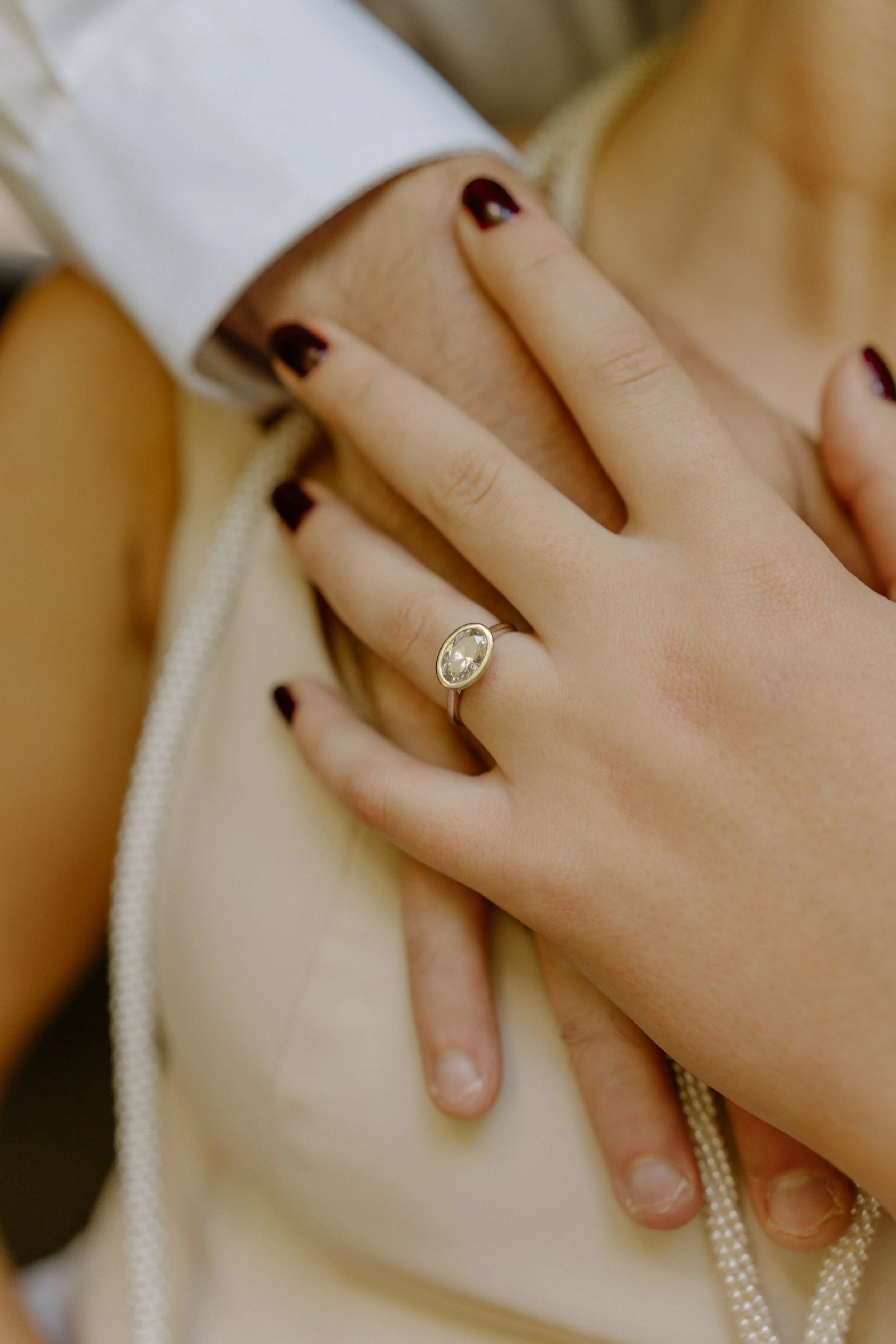A person wearing a ring with a large oval gemstone on their finger, resting their hand on another person's shoulder.