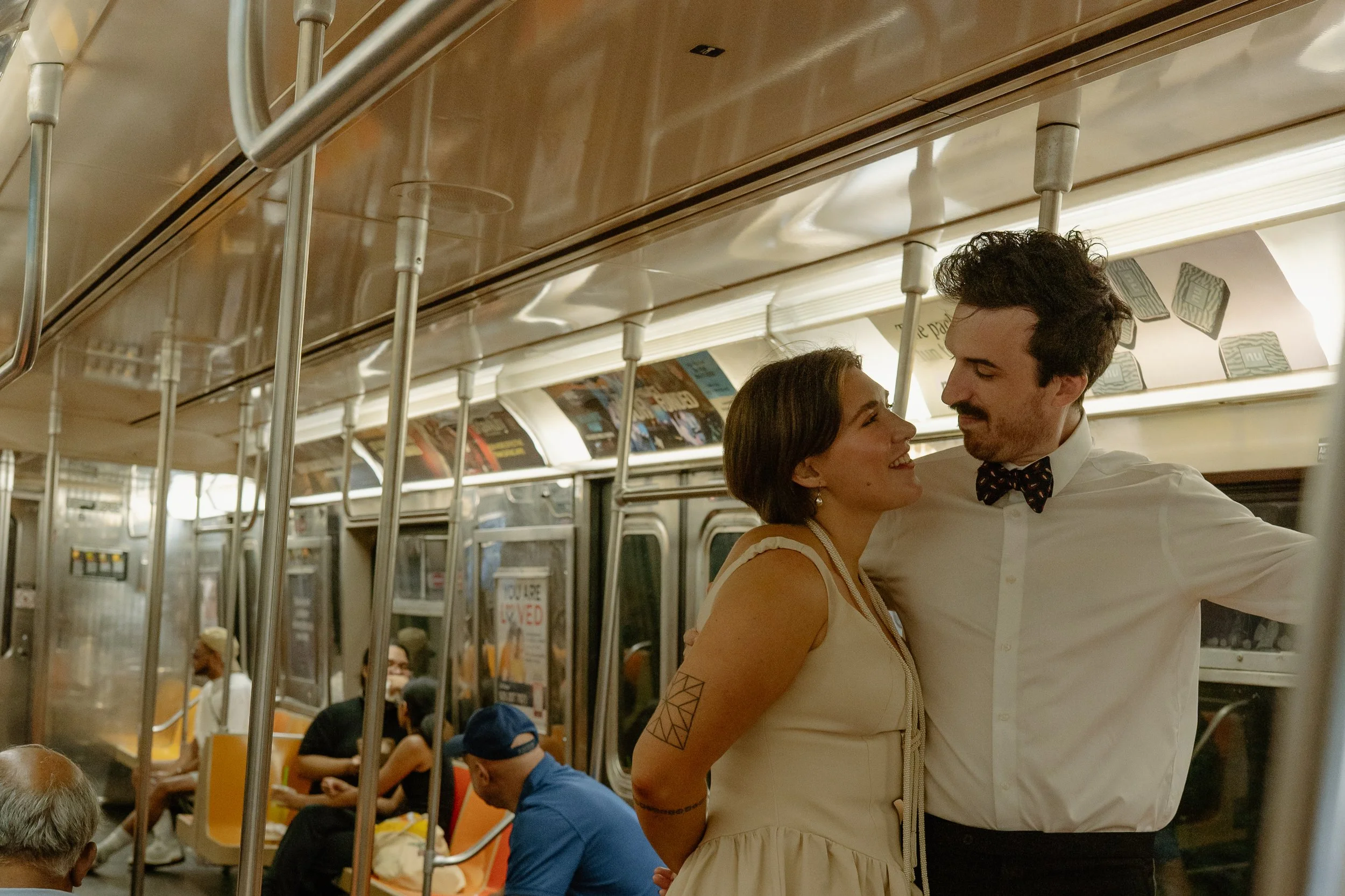 A couple dancing closely on a subway train, with the woman smiling and the man looking into her eyes, surrounded by seated passengers.