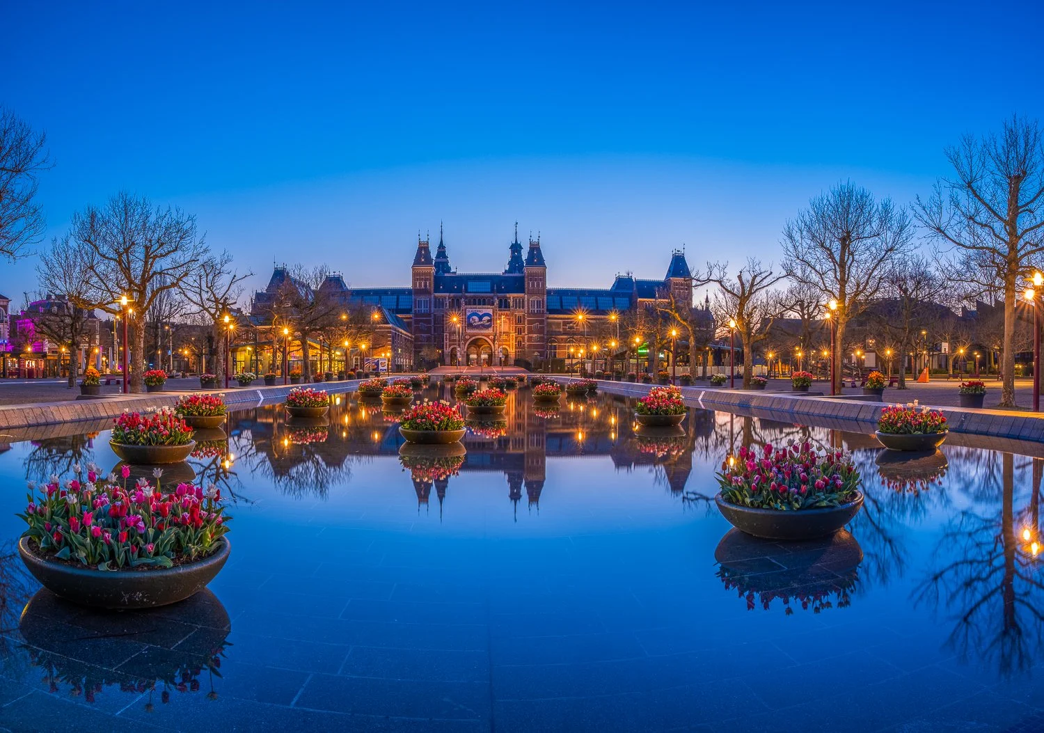 Stadsplein met bloemen, waterpartij en historisch gebouw bij schemerdonker in Nederland.