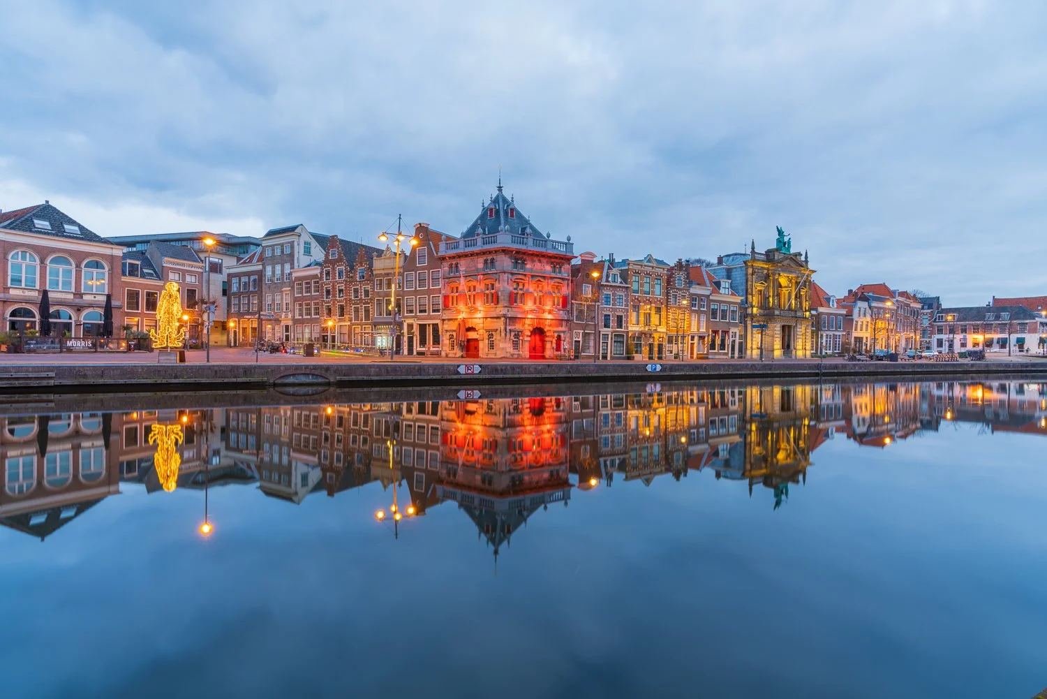 Een rivier met een stad op de achtergrond, verlichte historische gebouwen en een brug, met weerspiegeling in het water.