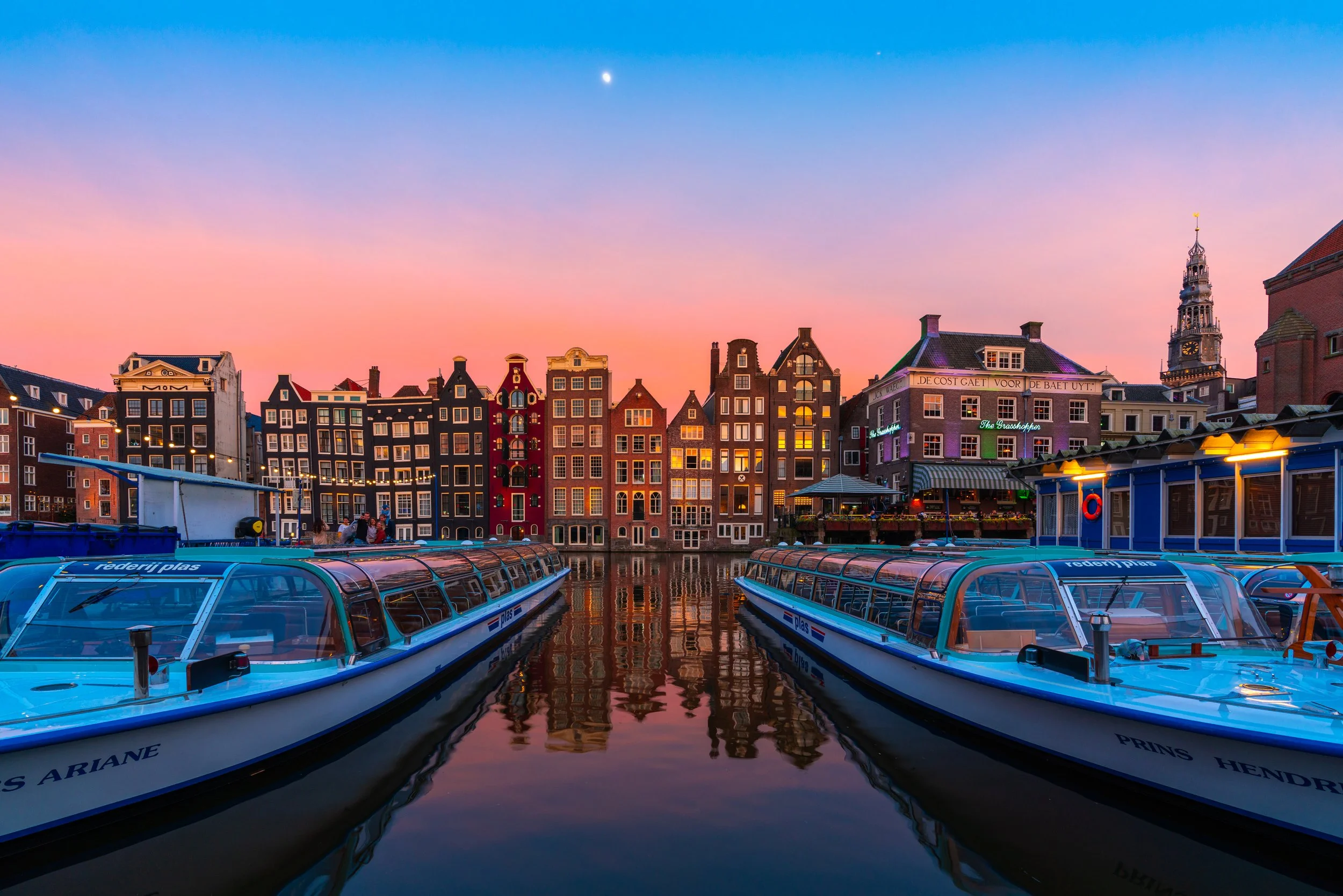Foto van de grachten in Amsterdam tijdens zonsondergang met schepen voor kleurrijke historische grachtenhuizen