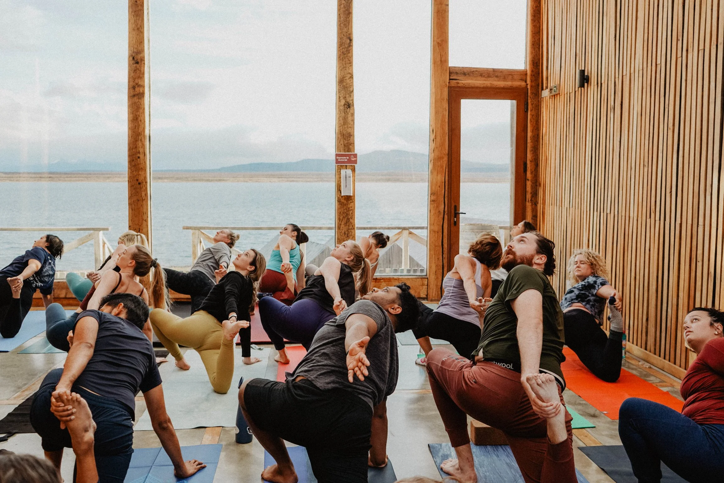 Group yoga class in wooden studio with large windows overlooking a lake.