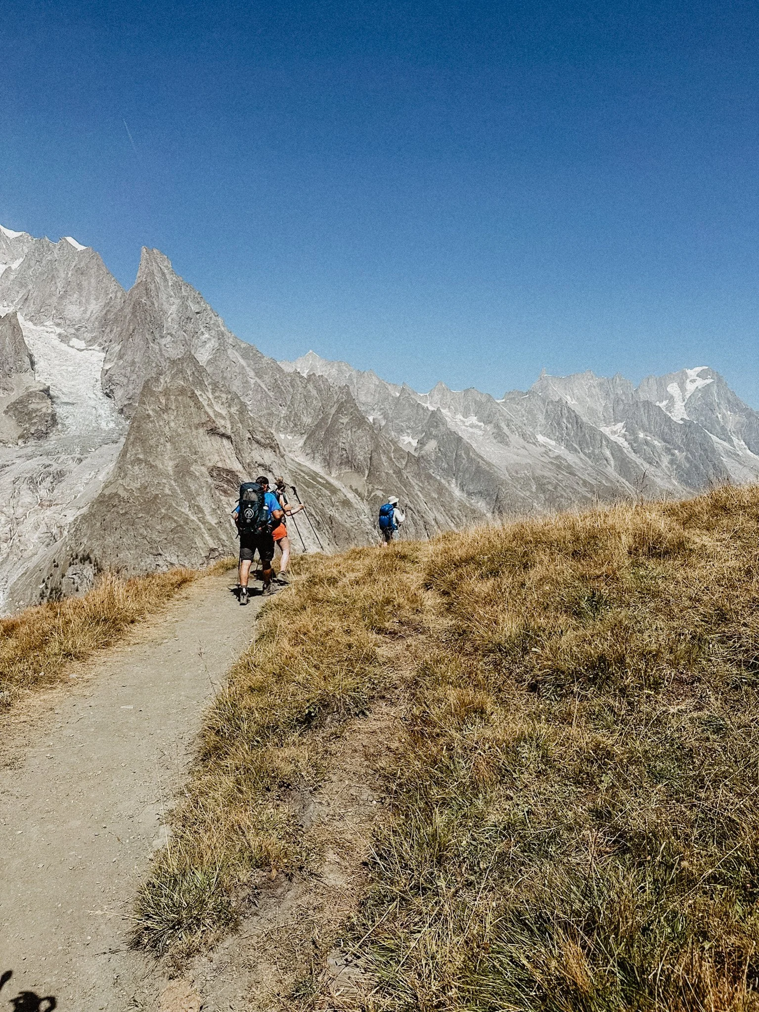 Hikers on a mountain trail with rocky peaks and blue sky