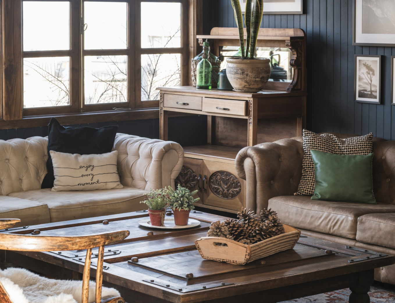 Cozy living room with wooden furniture, tan tufted sofas, a rustic coffee table, decorative plants, and framed wall art.