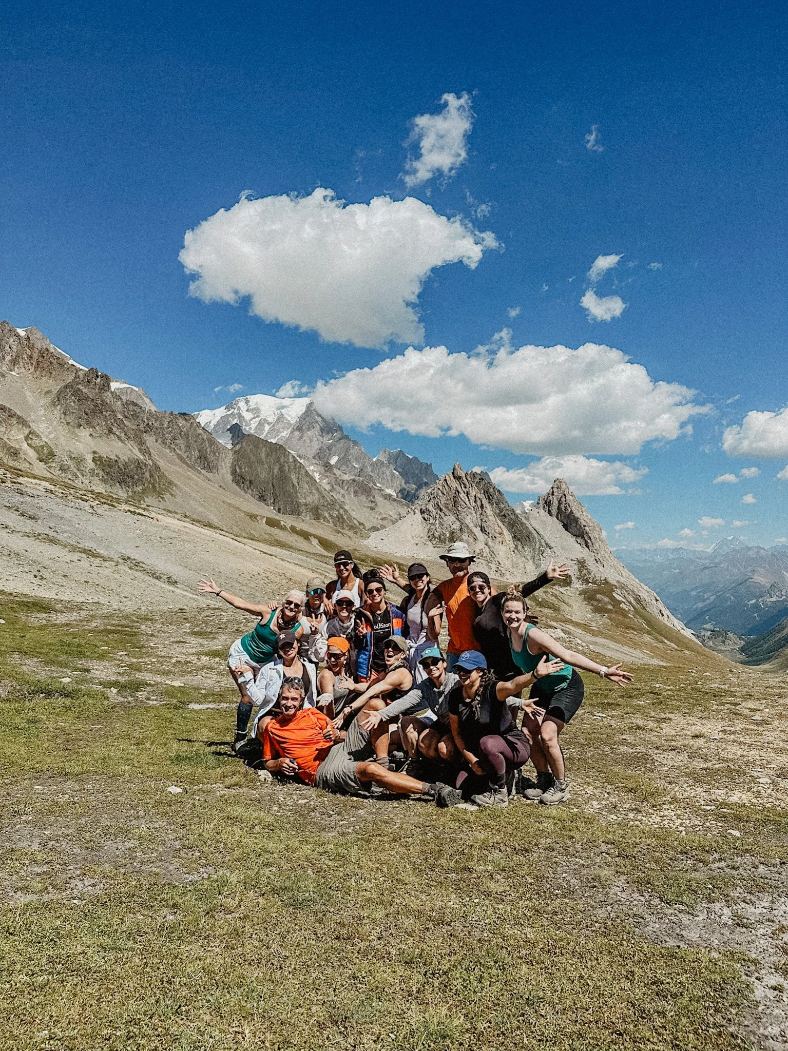 Group of people posing on a mountain landscape with blue sky and clouds in the background.