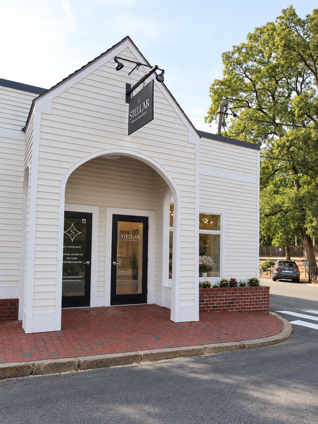 White building with black signs reading 'Stellar Medical Aesthetics' and storefront windows, brick sidewalk, and trees in the background.