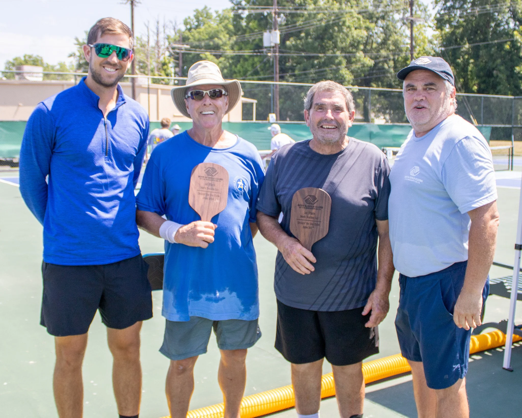 Four men on a tennis court holding plaques, dressed in sportswear, celebrating at a tennis event.
