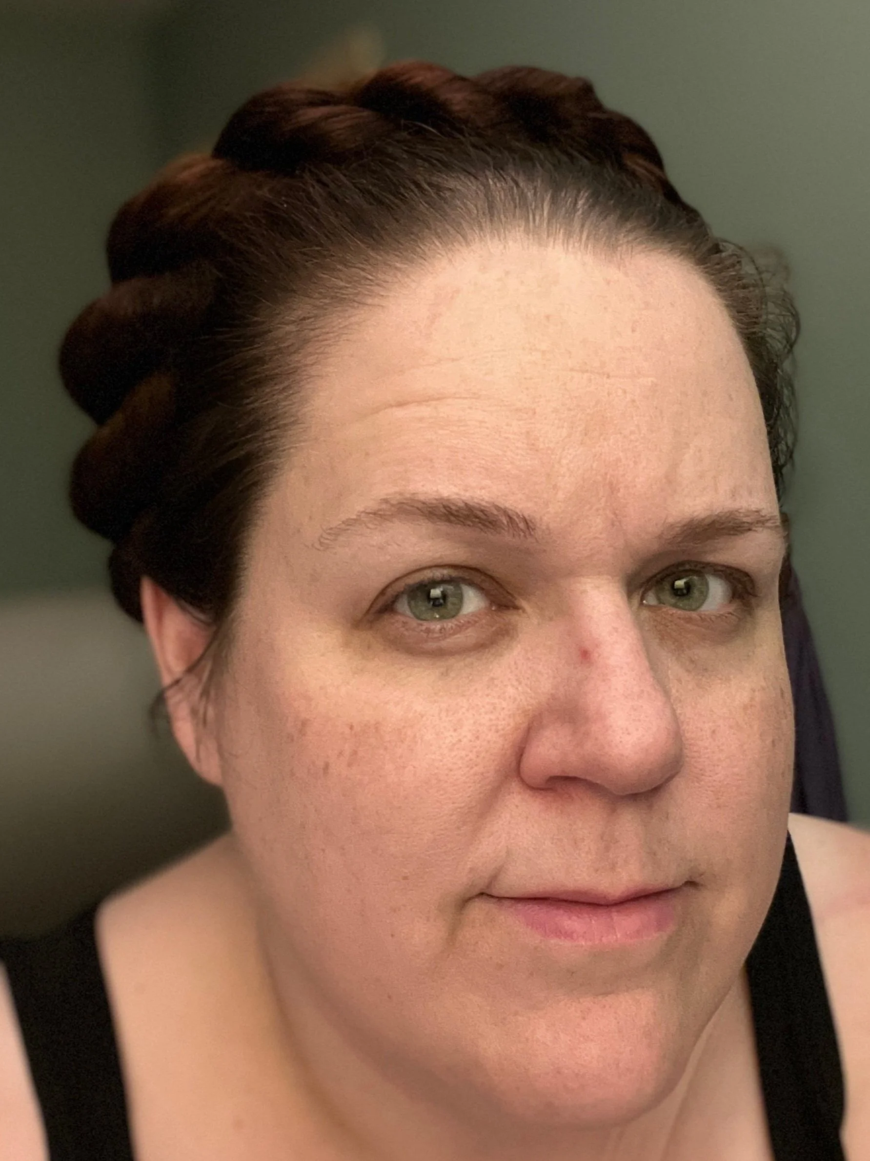 Close-up of a person's face with light skin, green eyes, freckles, and dark brown hair styled in a crown braid.