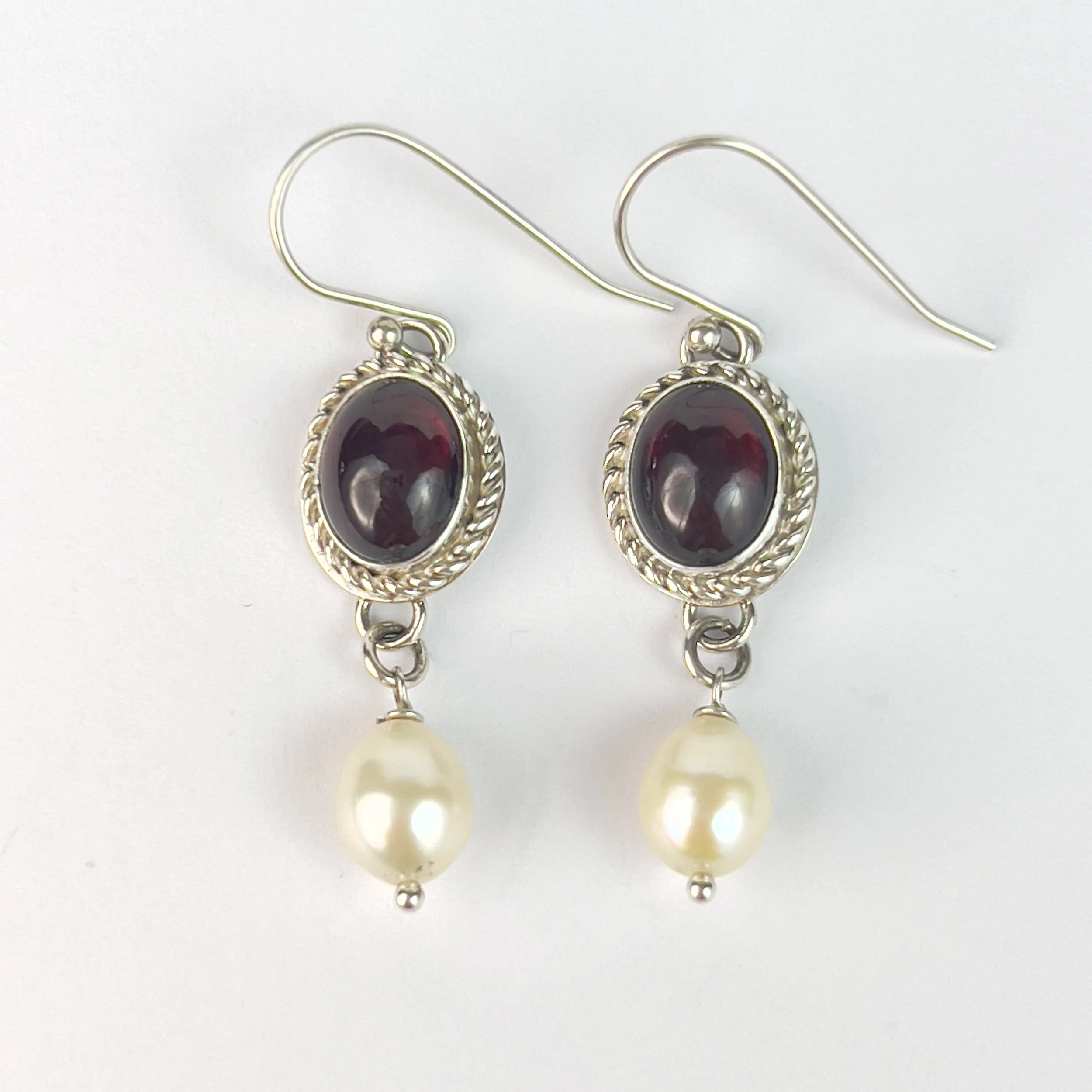Silver earrings with oval garnet stones and dangling cream-colored pearls.