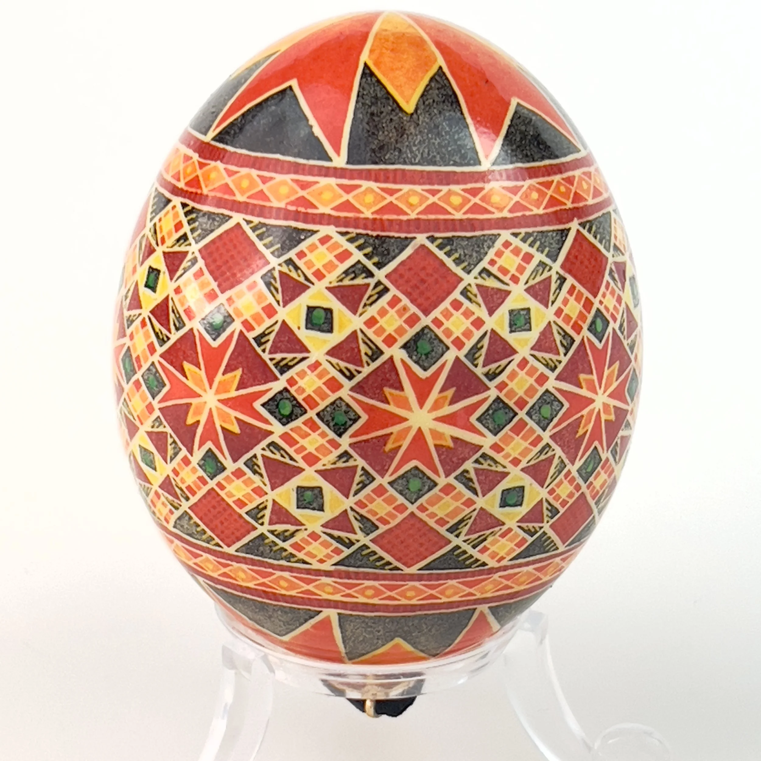 Decorative egg with intricate geometric patterns in red, black, yellow, and green on a white background.