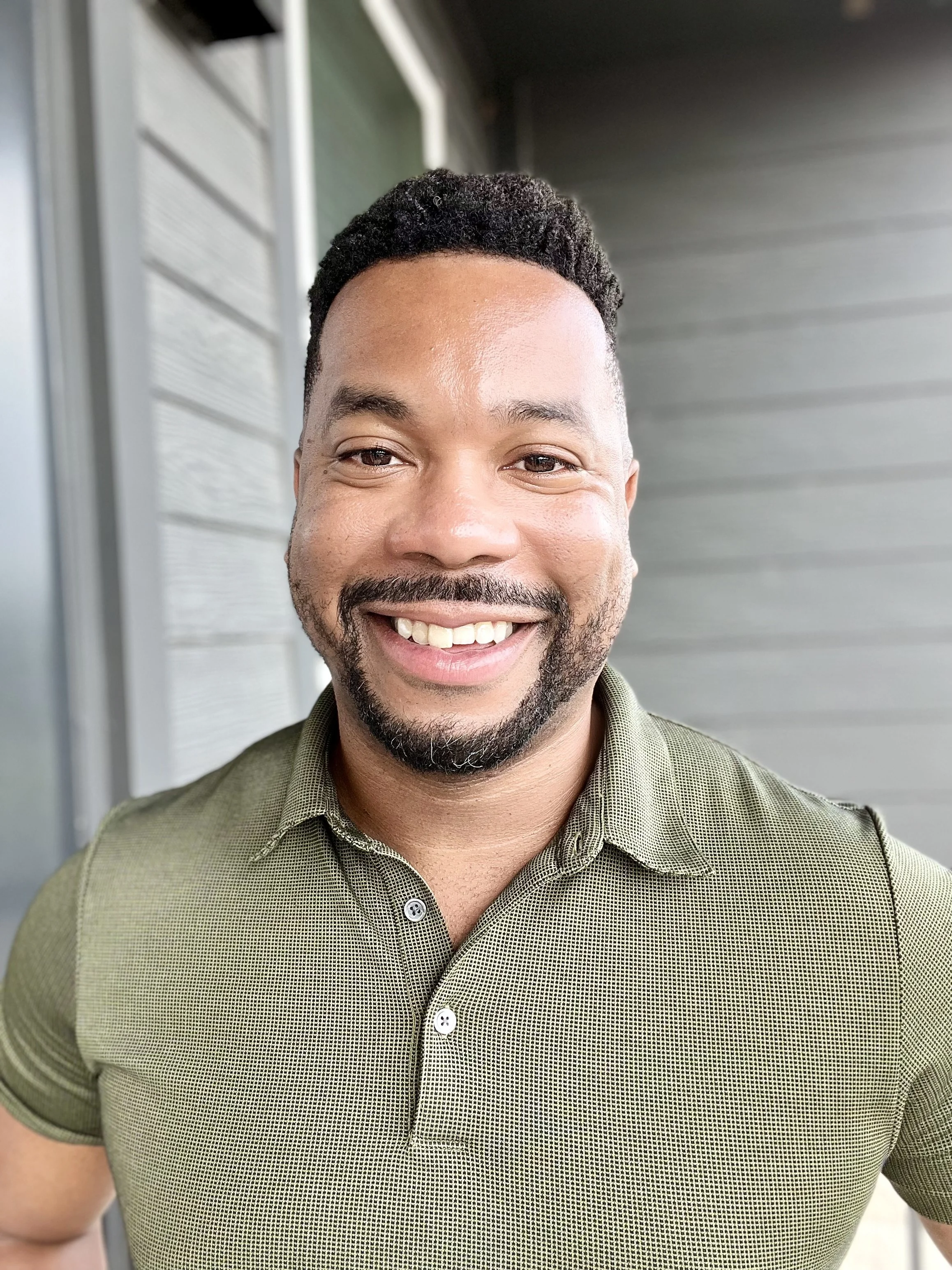 A photo of Travers smiling with a green shirt that has a collar. He has a beard.