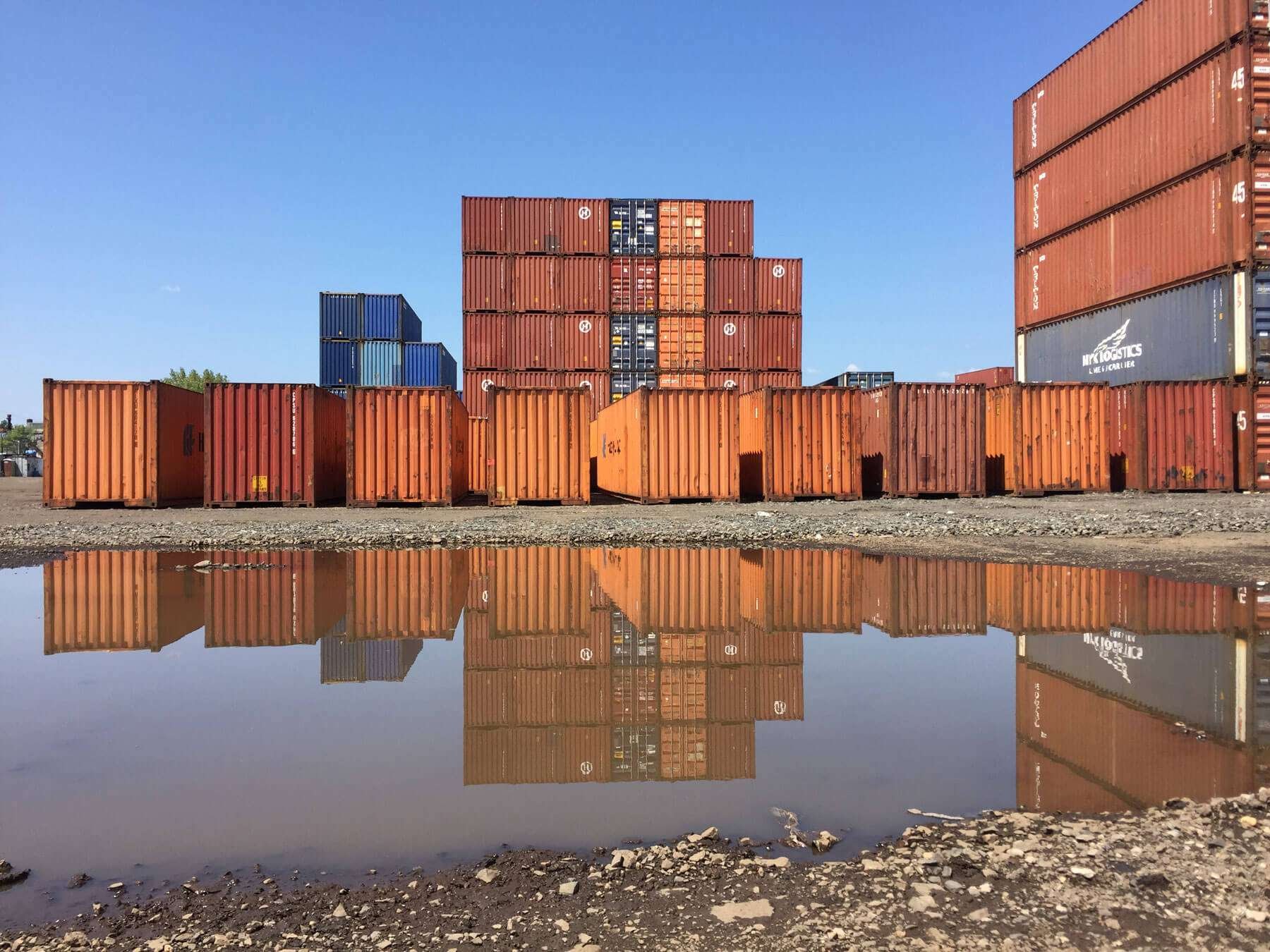  Stacks of shipping containers and their reflection in a puddle. 