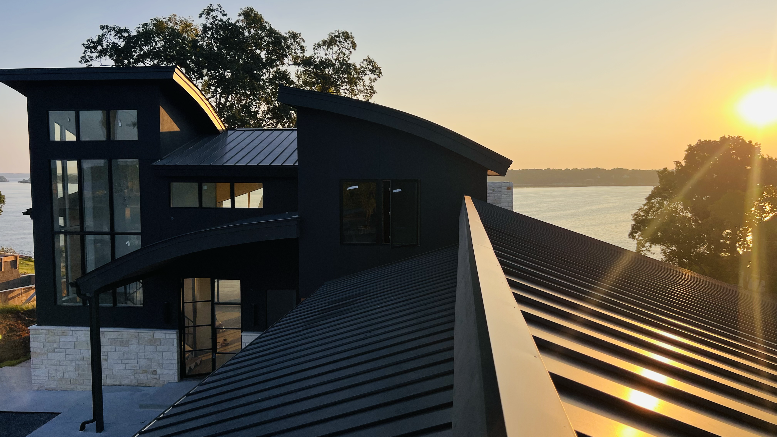 Standing-seam metal roof beside a modern glazed tower at sunset.