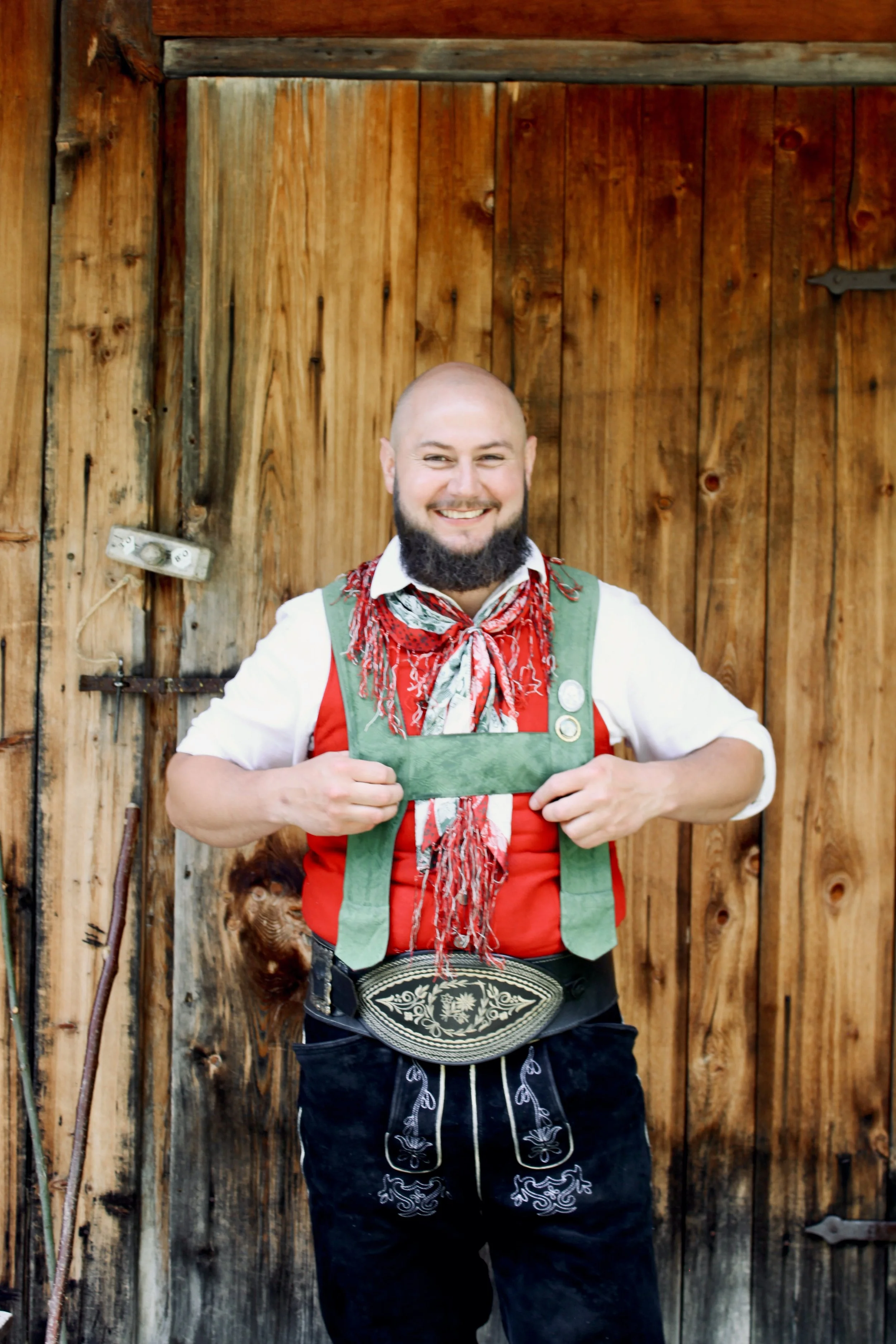 Mann mit Bart, in traditioneller Tracht, vor einem Vorhang.