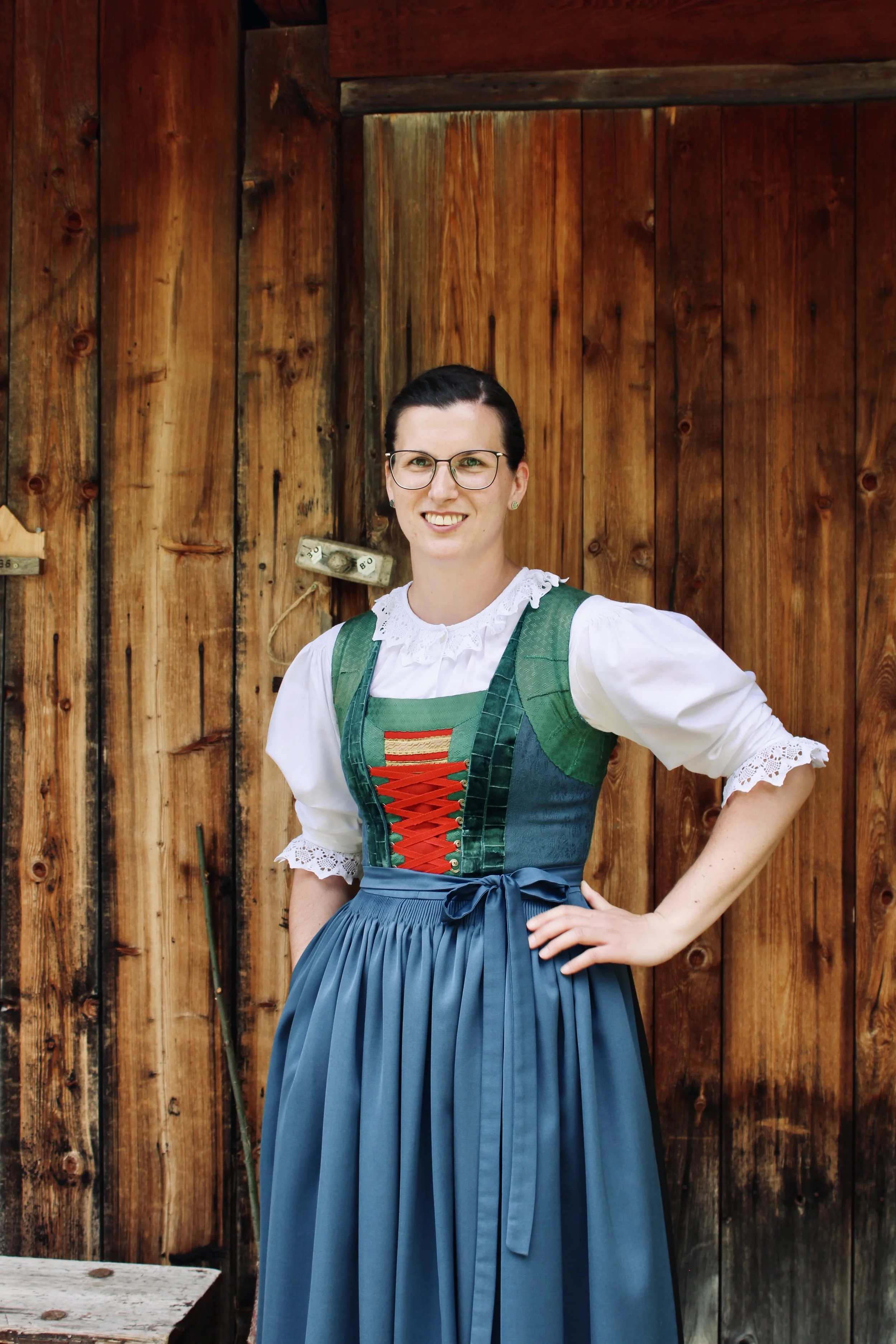 Ein lächelnder Mann mit rotem und weißen Outfit, braunem Haar und Bart, vor grauen Vorhängen. /