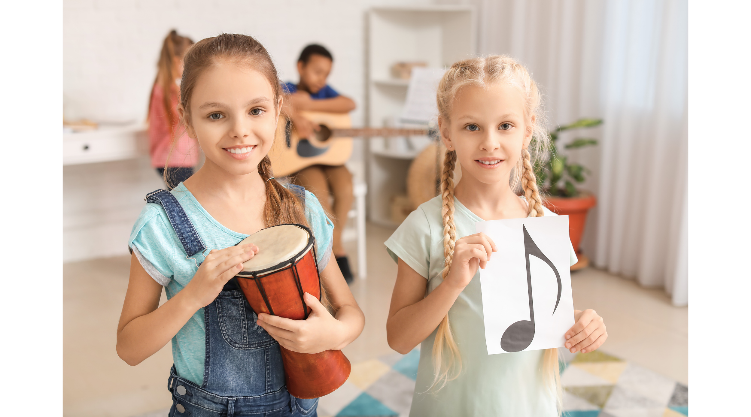 Two young girls smiling and holding musical items, with one girl holding a small drum and the other holding a sheet of paper with a musical note, while children in the background are playing guitar and standing near a white shelf.