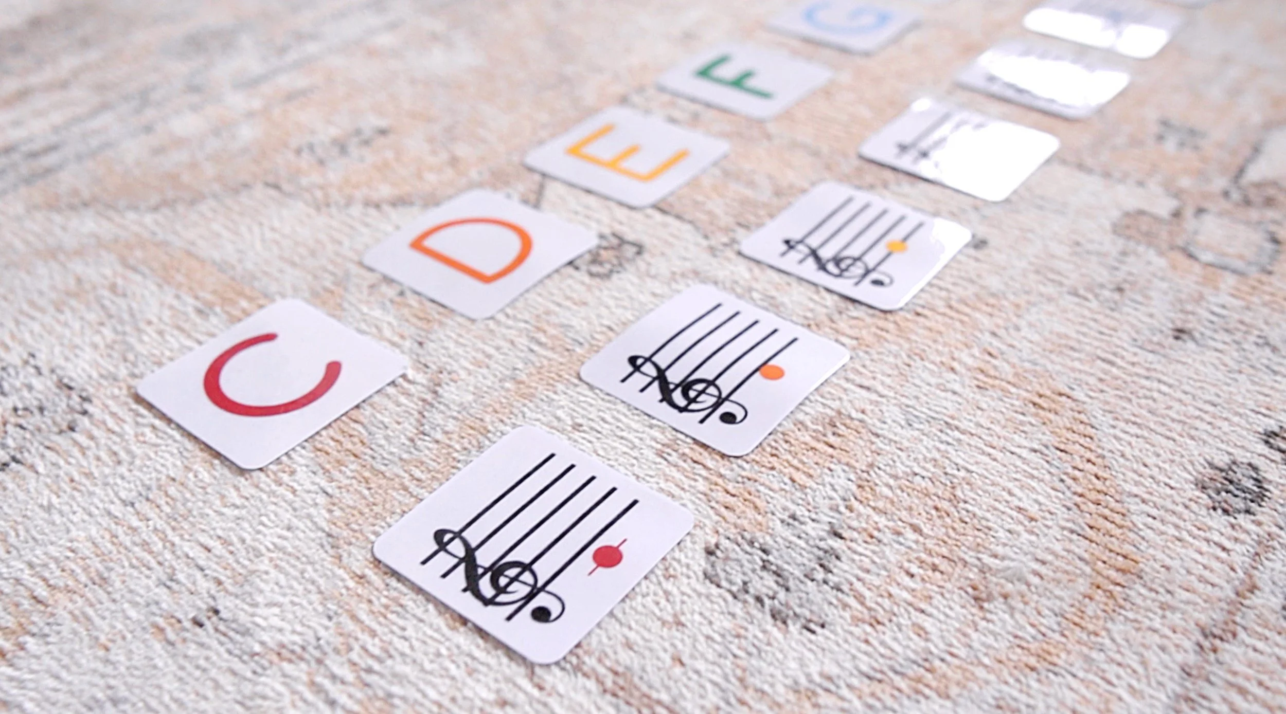 Close-up of cards with letters and musical notes on a textured rug.