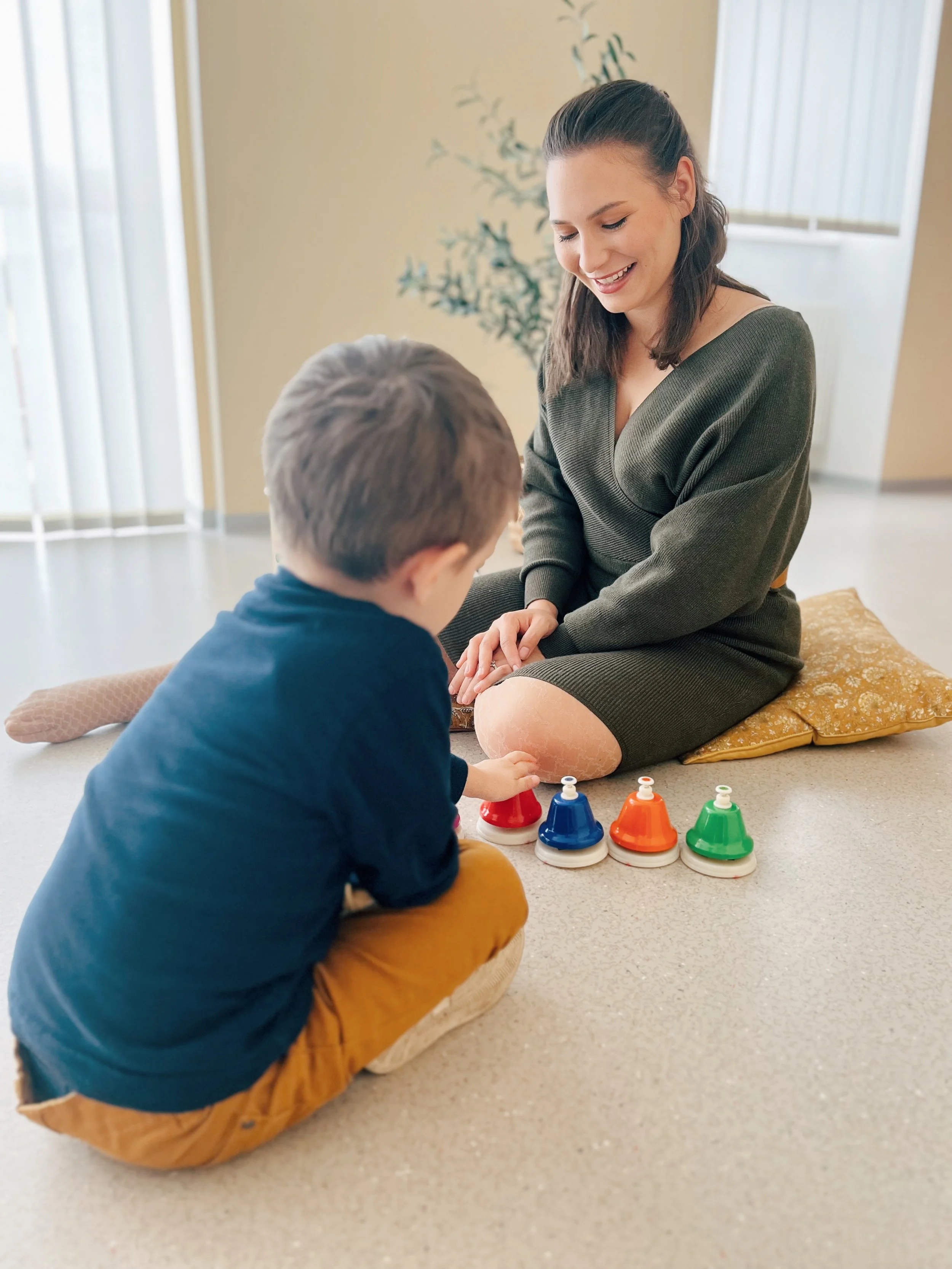 A woman and a young boy playing a game with colorful bells on the floor in a bright room.