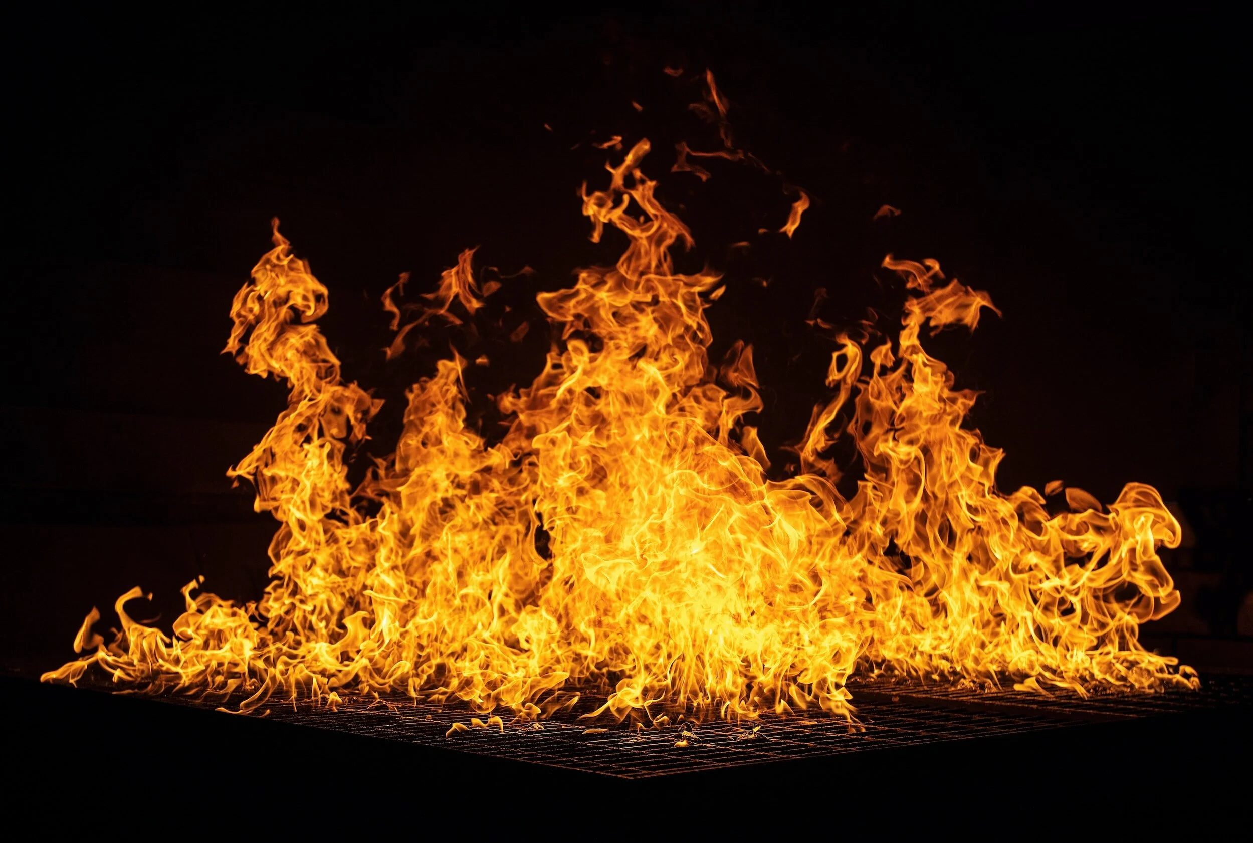Large flames erupting from a fire on a grill against a dark background.