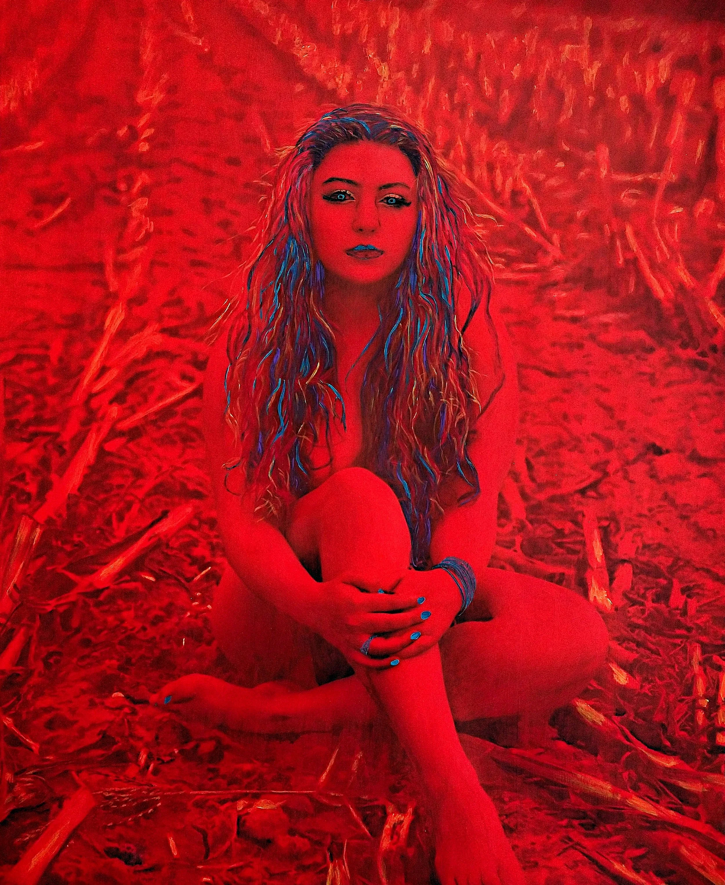 A woman with long, wavy hair sitting on the ground amidst grass or straw, with a red filter overlay.