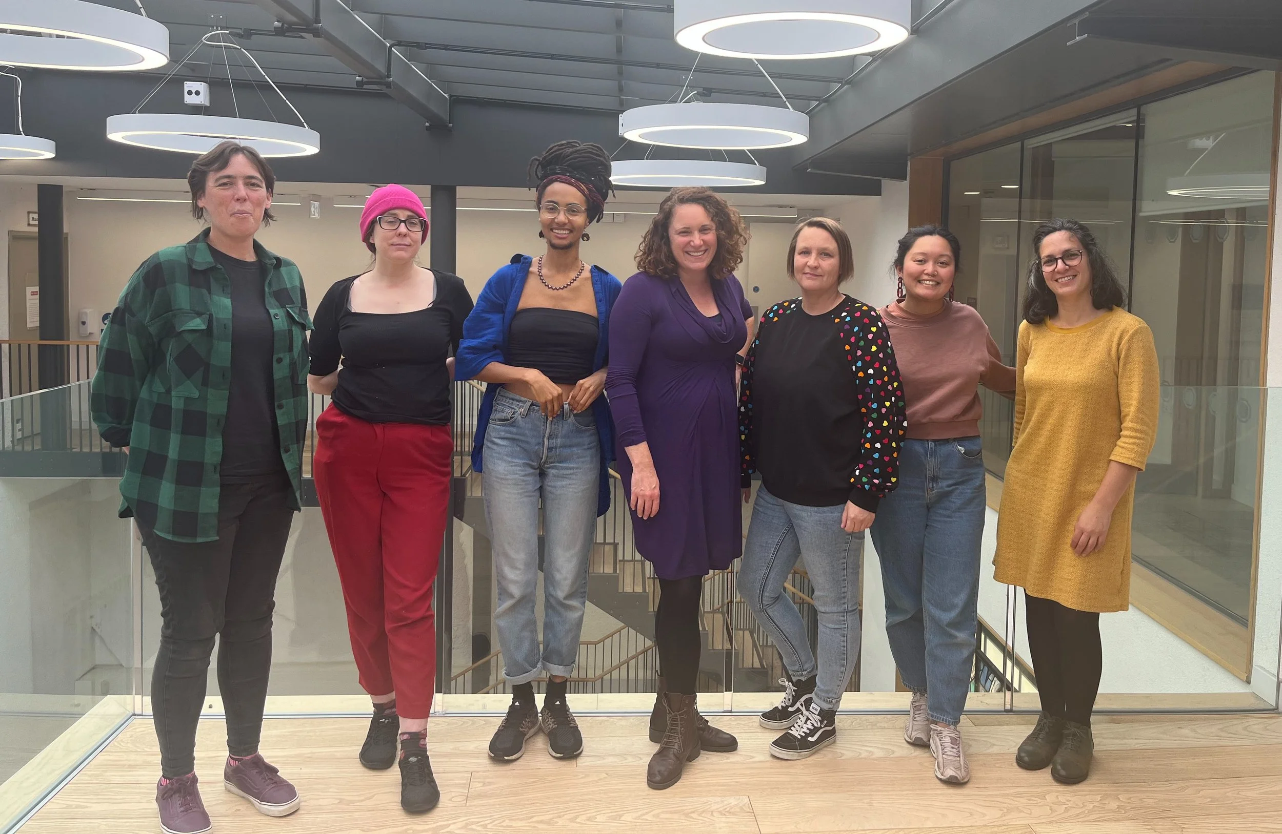 Seven of the panel members, standing in a line and smiling at the camera.