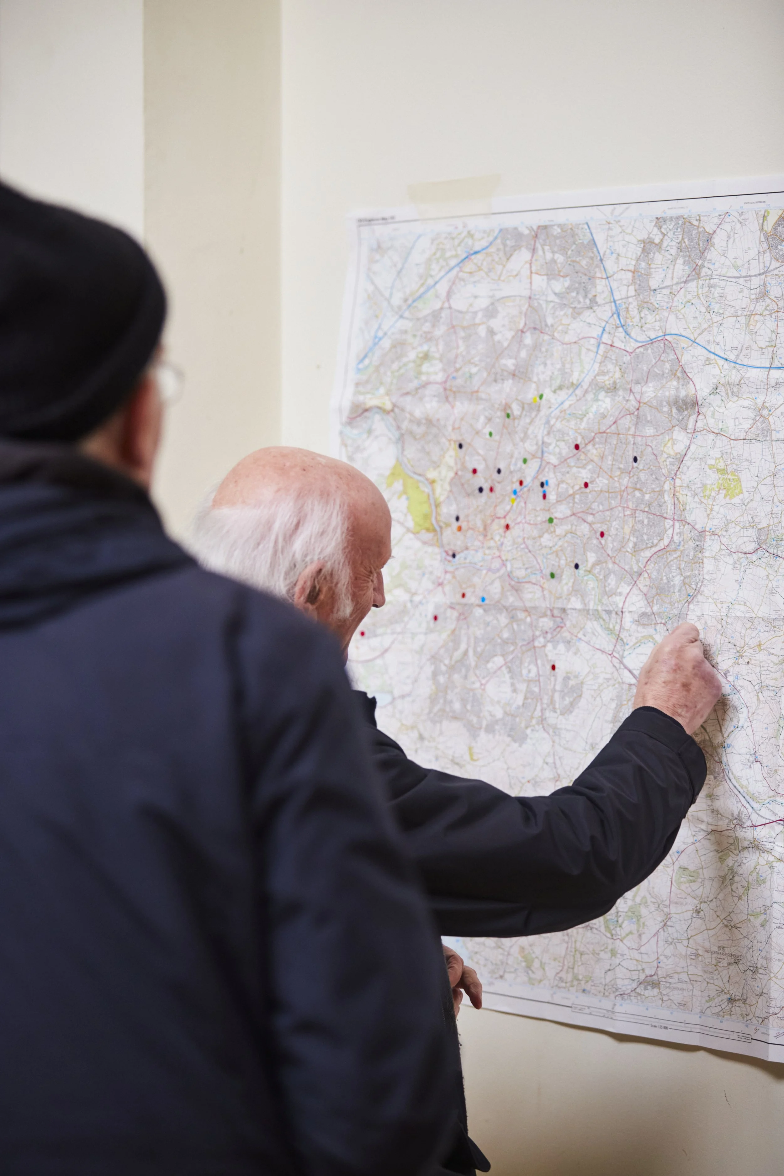 A man sticks a coloured dot to a map of Bristol which is hanging from the wall. The map already has about 25 dots on it.