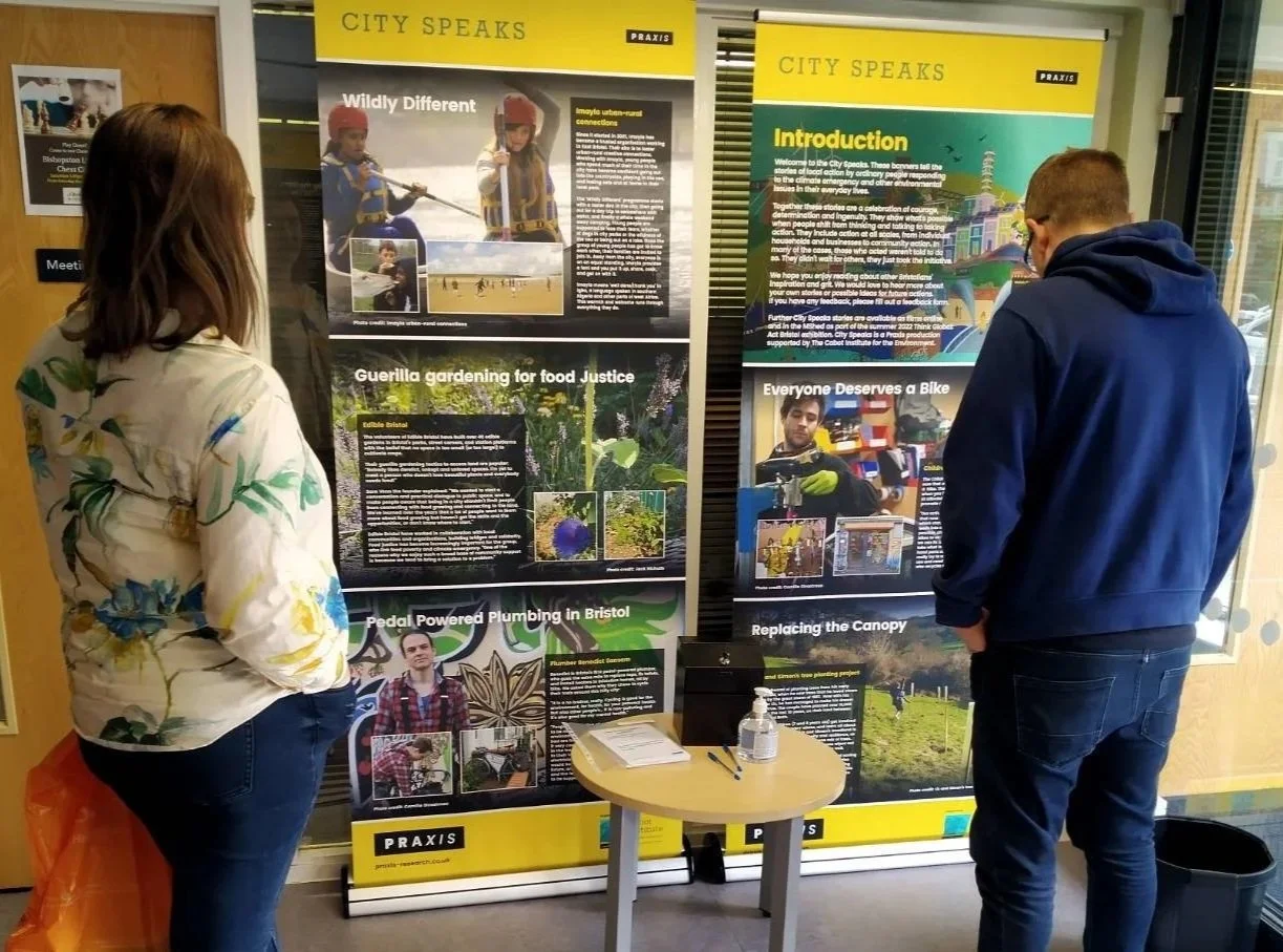 Photo of two residents standing, looking at a City Speaks exhibition in J3 Library in Bristol. The exhibition celebrates environmental action by residents. 
