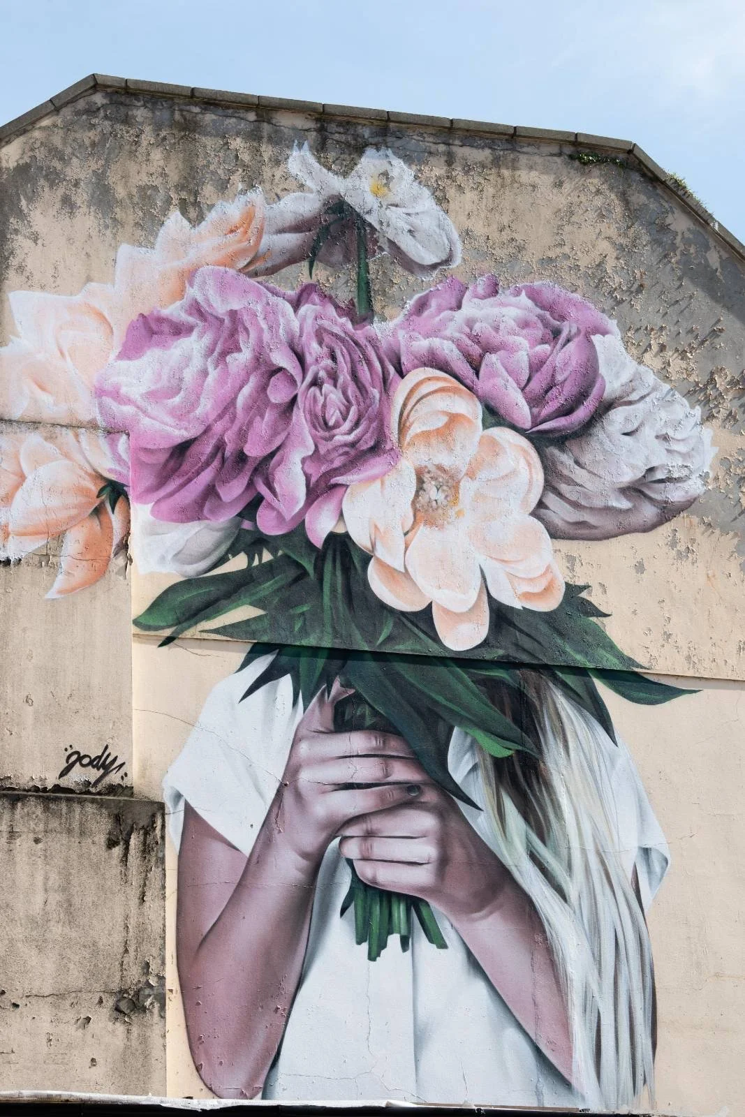 Bristol landmark of graffiti on a wall of a person holding up a bouquet of flowers over their face.
