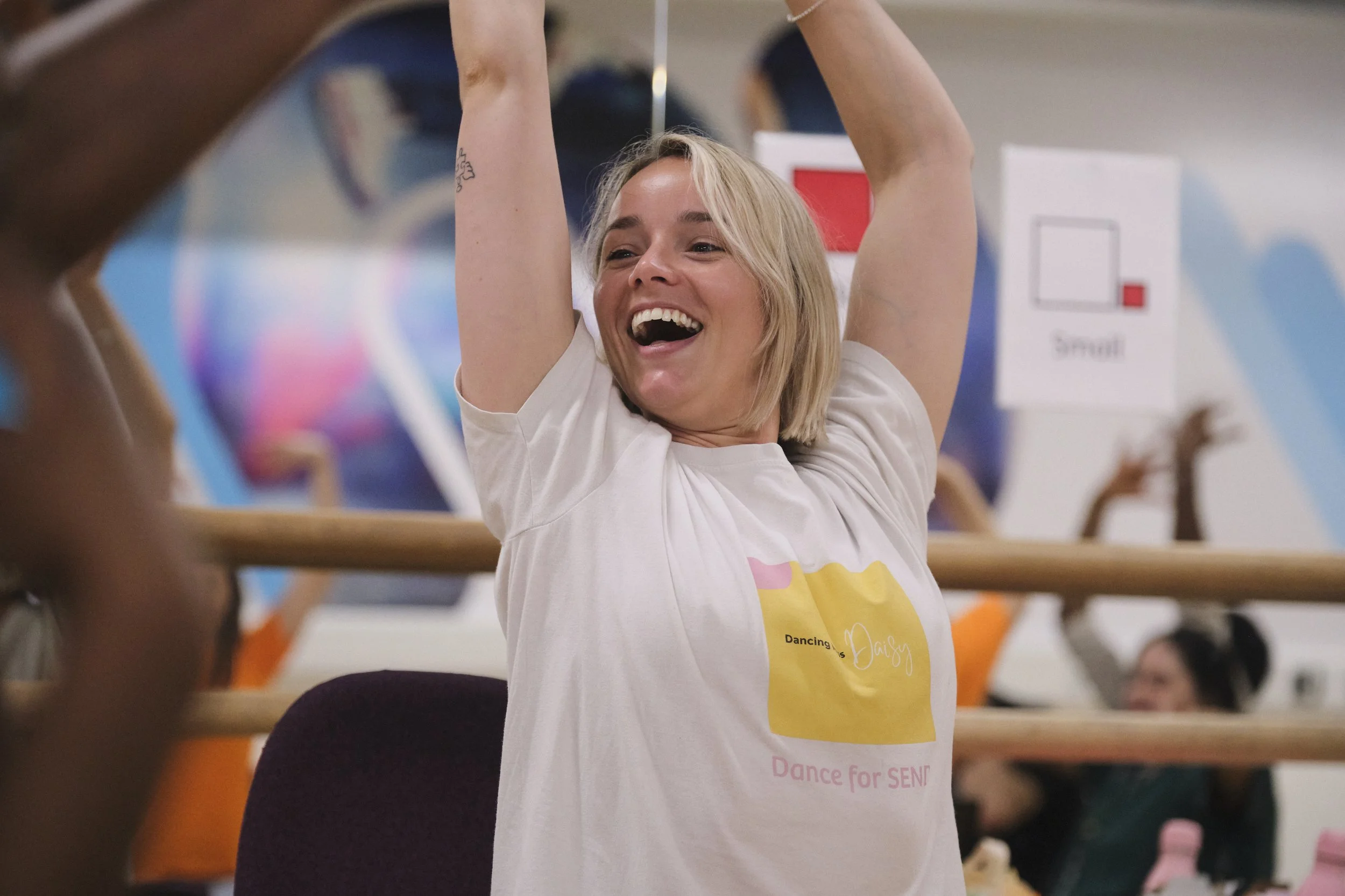 A lady in white with blonde hair smiles, raising her arms above her head