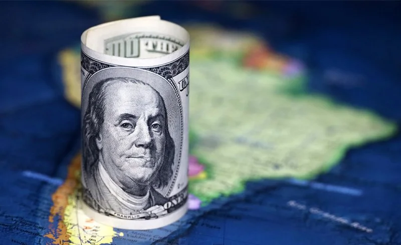 Rolled U.S. hundred-dollar bill on a world map background.