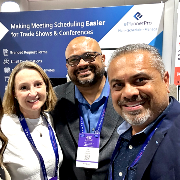 Three people smiling at a trade show booth with a blue banner displaying 'Making Meeting Scheduling Easier for Trade Shows & Conferences' and 'ePlannerPro' logo in the background.