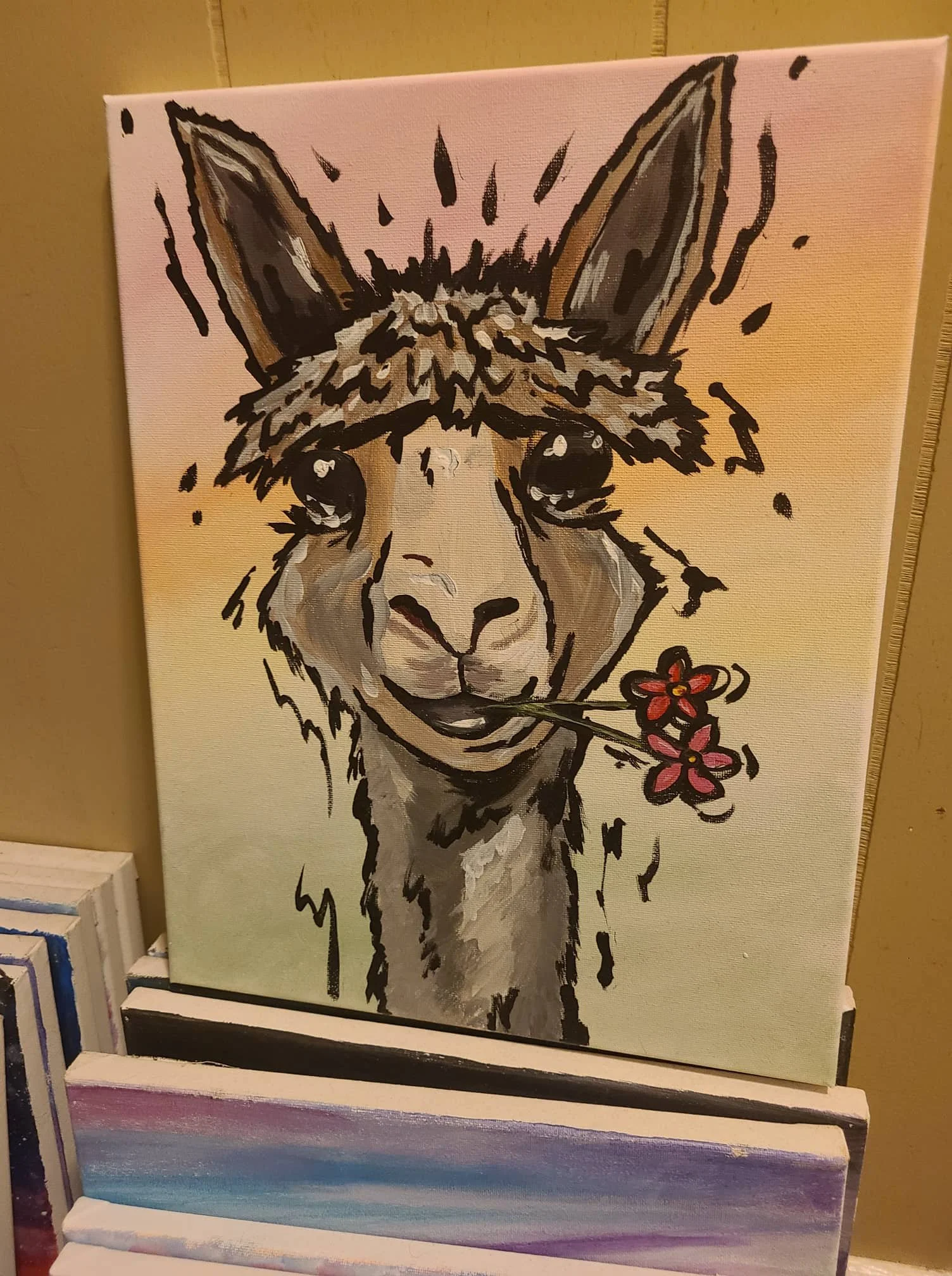 Canvas painting of fawn colored alpaca with two red flowers in it's mouth.