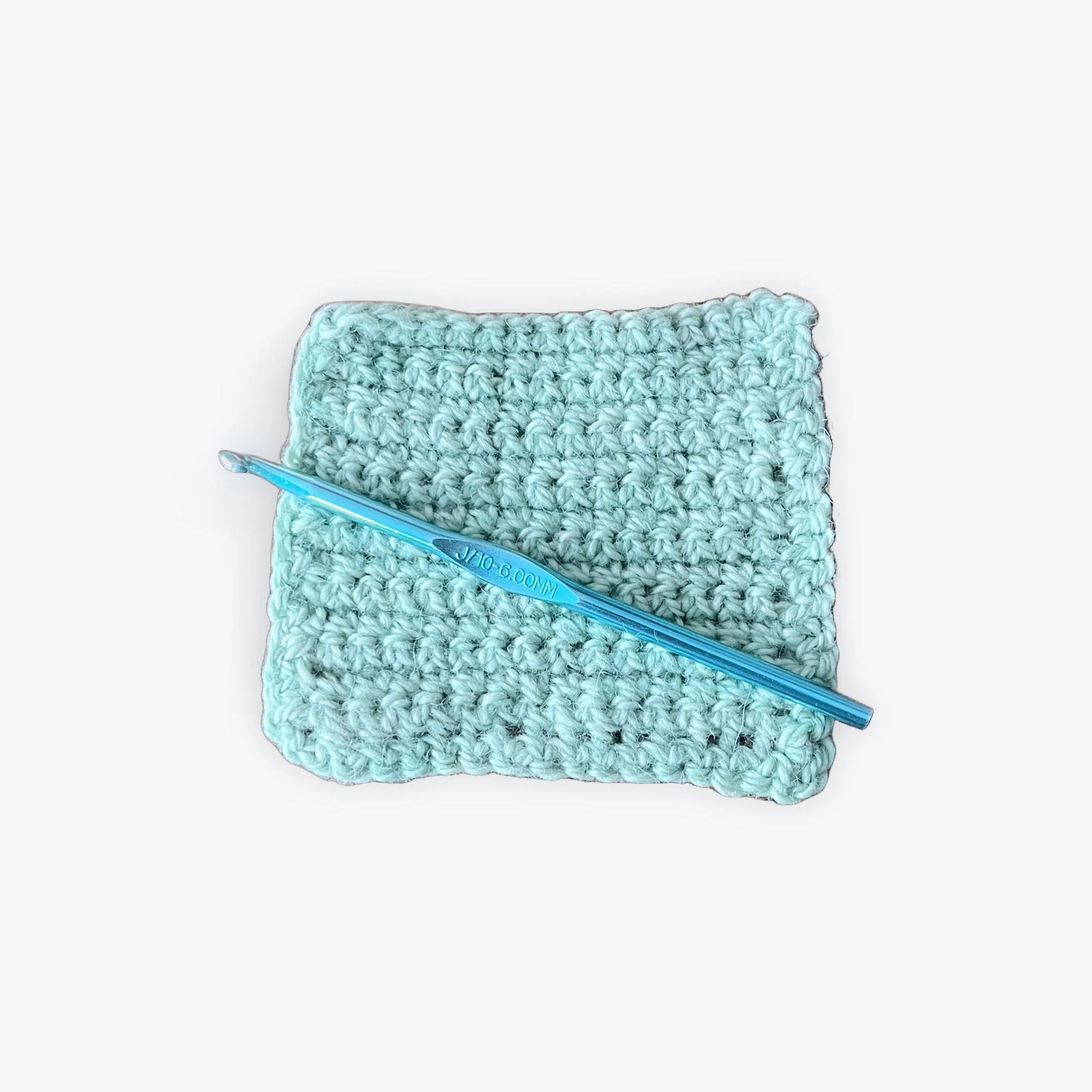 Flat mint green crochet square with blue crochet hook on top