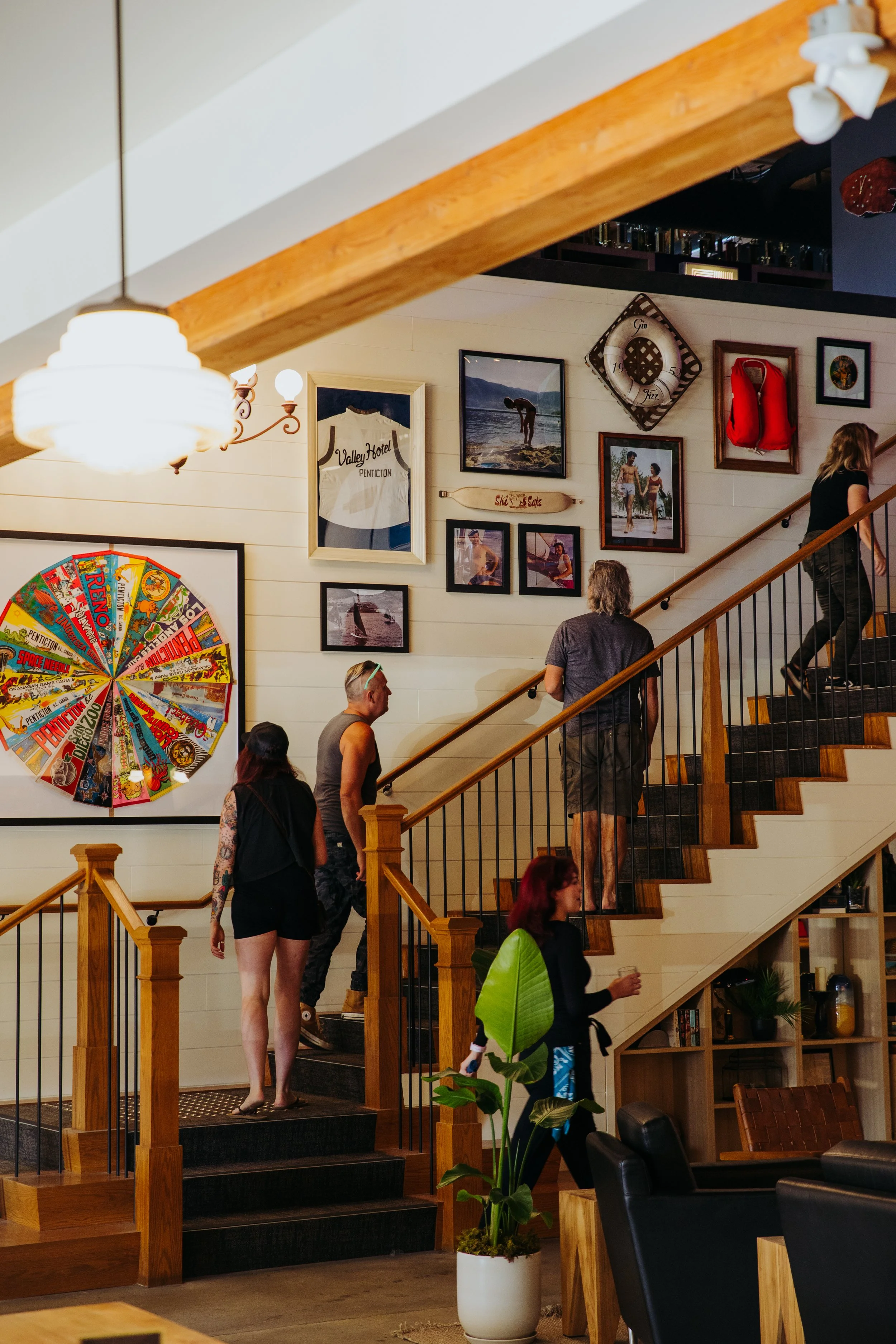People ascending a staircase inside a cozy, decorated hotel or cafe with framed pictures and artwork on the wall.