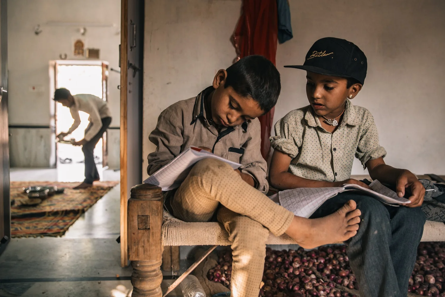 Two boys sit reading on a charpoy in a doorway in India, sacks of onions at their feet — from the India series, Delhi to the Ganges
