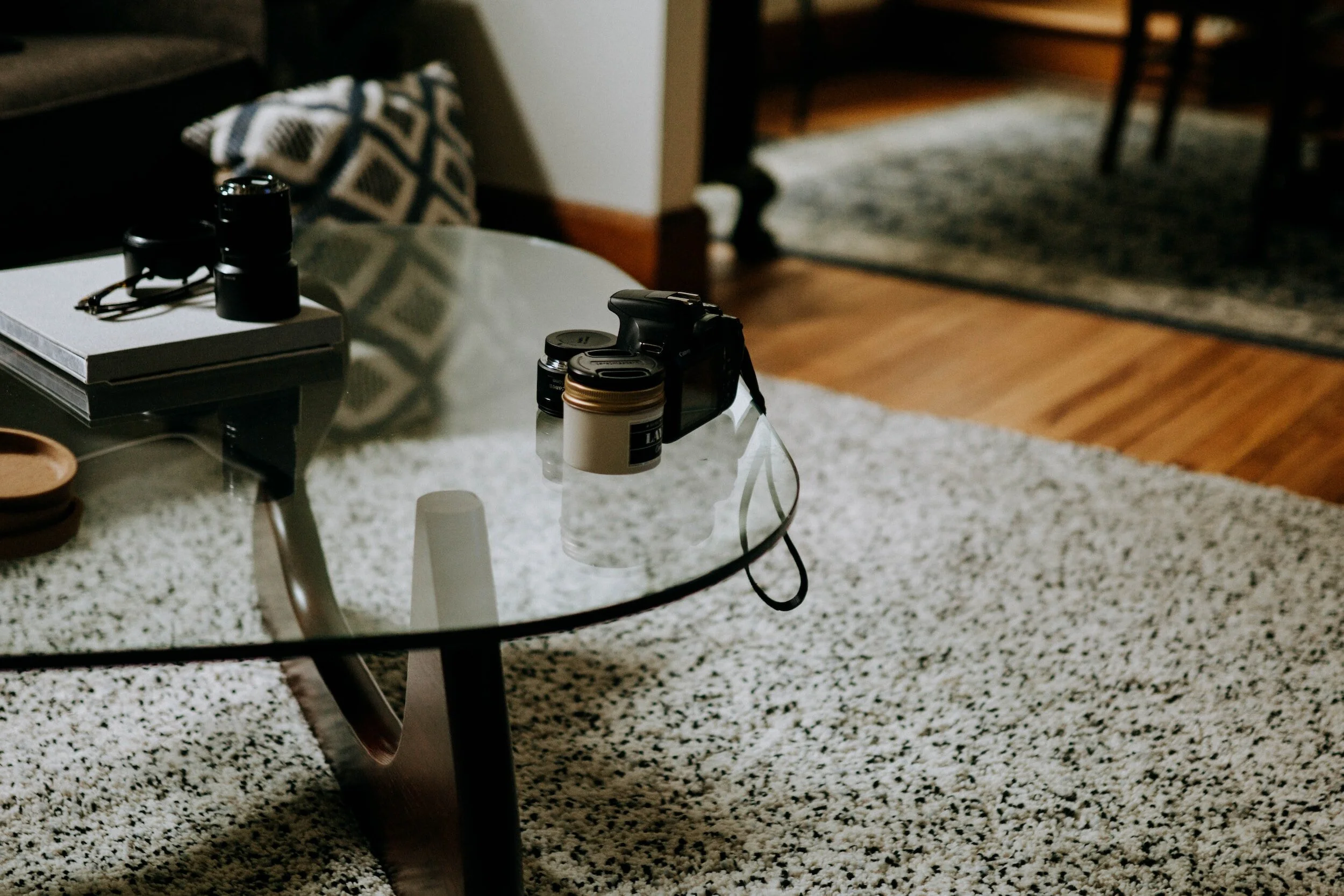 Interior of living room with glass coffee table, camera, lenses, and decorative items.