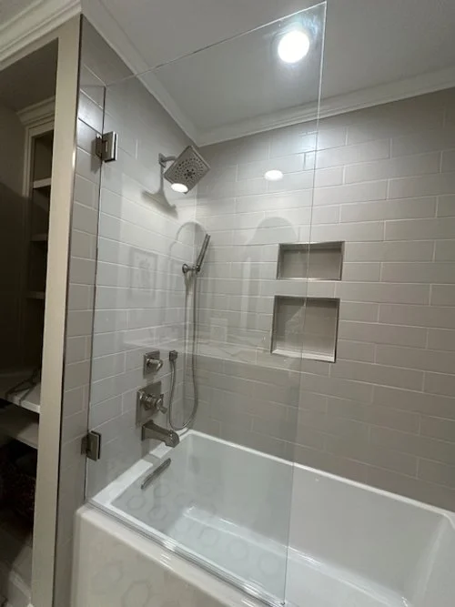 Modern bathroom with glass shower, white subway tiles, built-in shelves, and overhead showerhead.