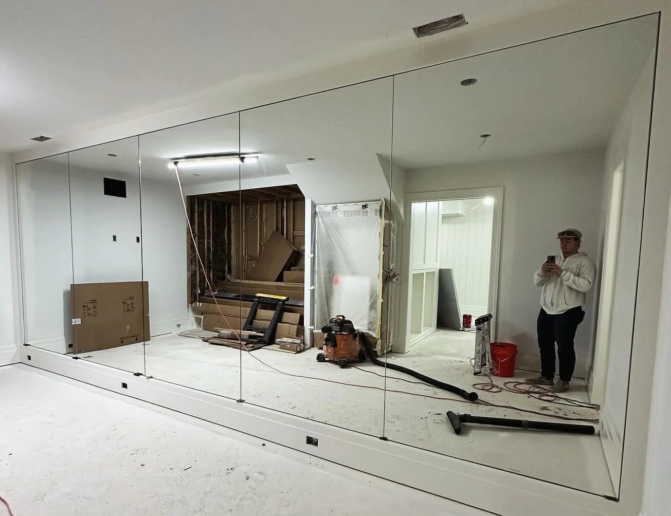 Room under construction with mirrored wall, construction materials, and a person taking a selfie.