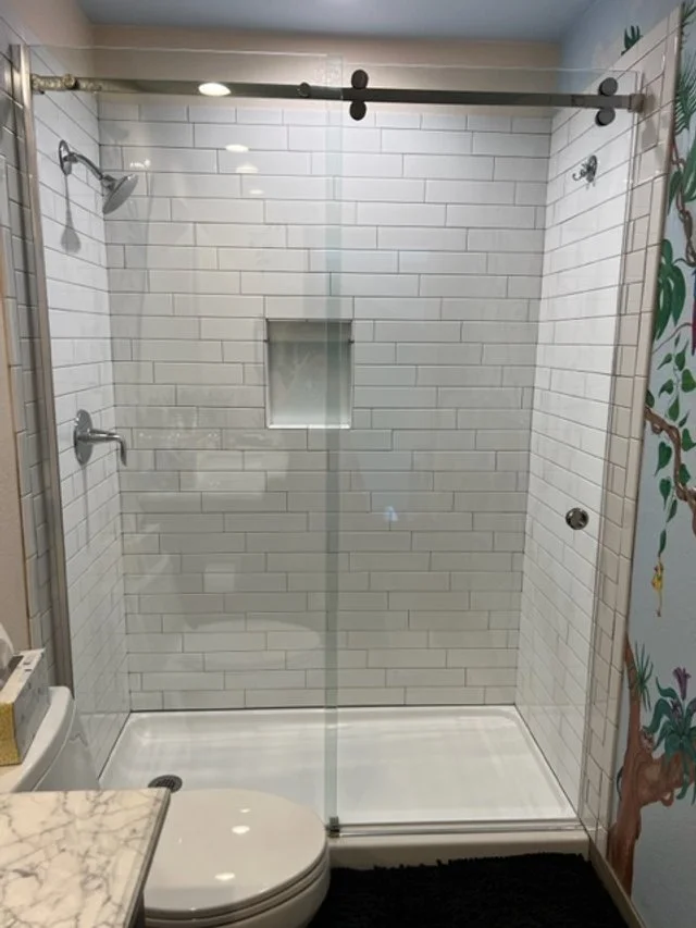 Modern bathroom with a glass shower enclosure, white subway tiles, built-in shower niche, and decorative mural on the wall.