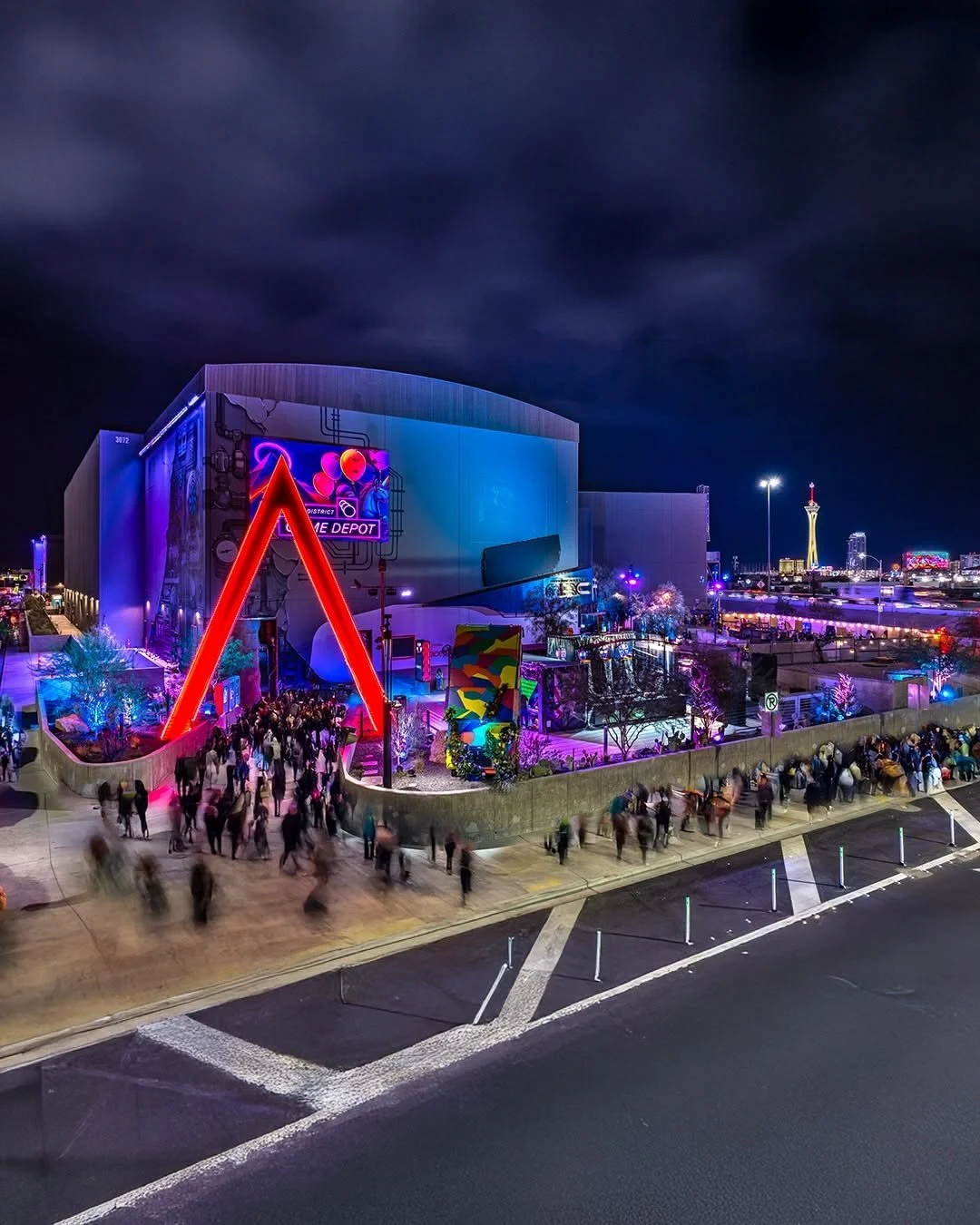 Night view of a colorful indoor entertainment complex with neon lights and a crowd of people outside.