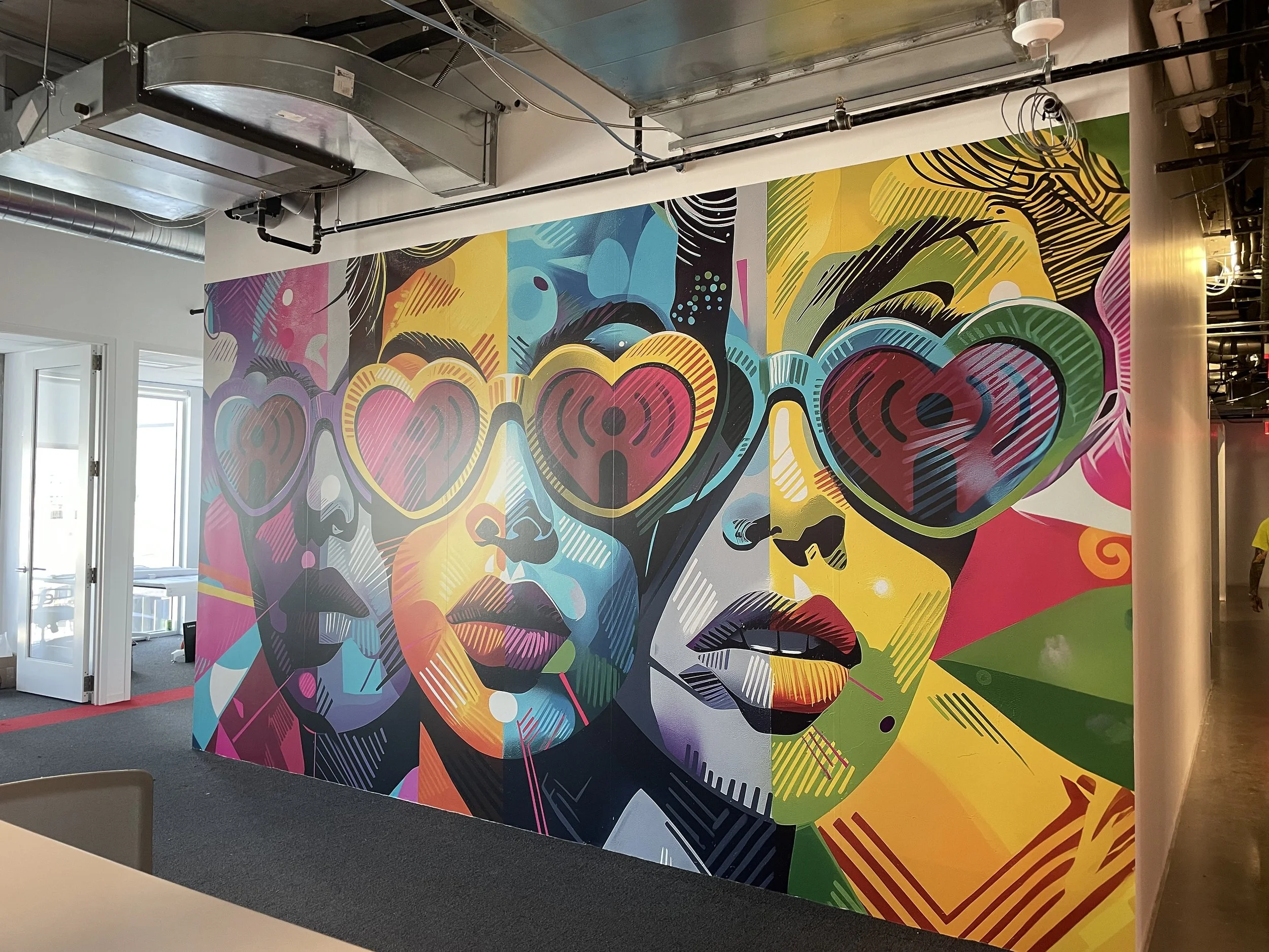Colorful mural of three women with heart-shaped sunglasses, depicted in a pop art style with vivid colors and bold lines.