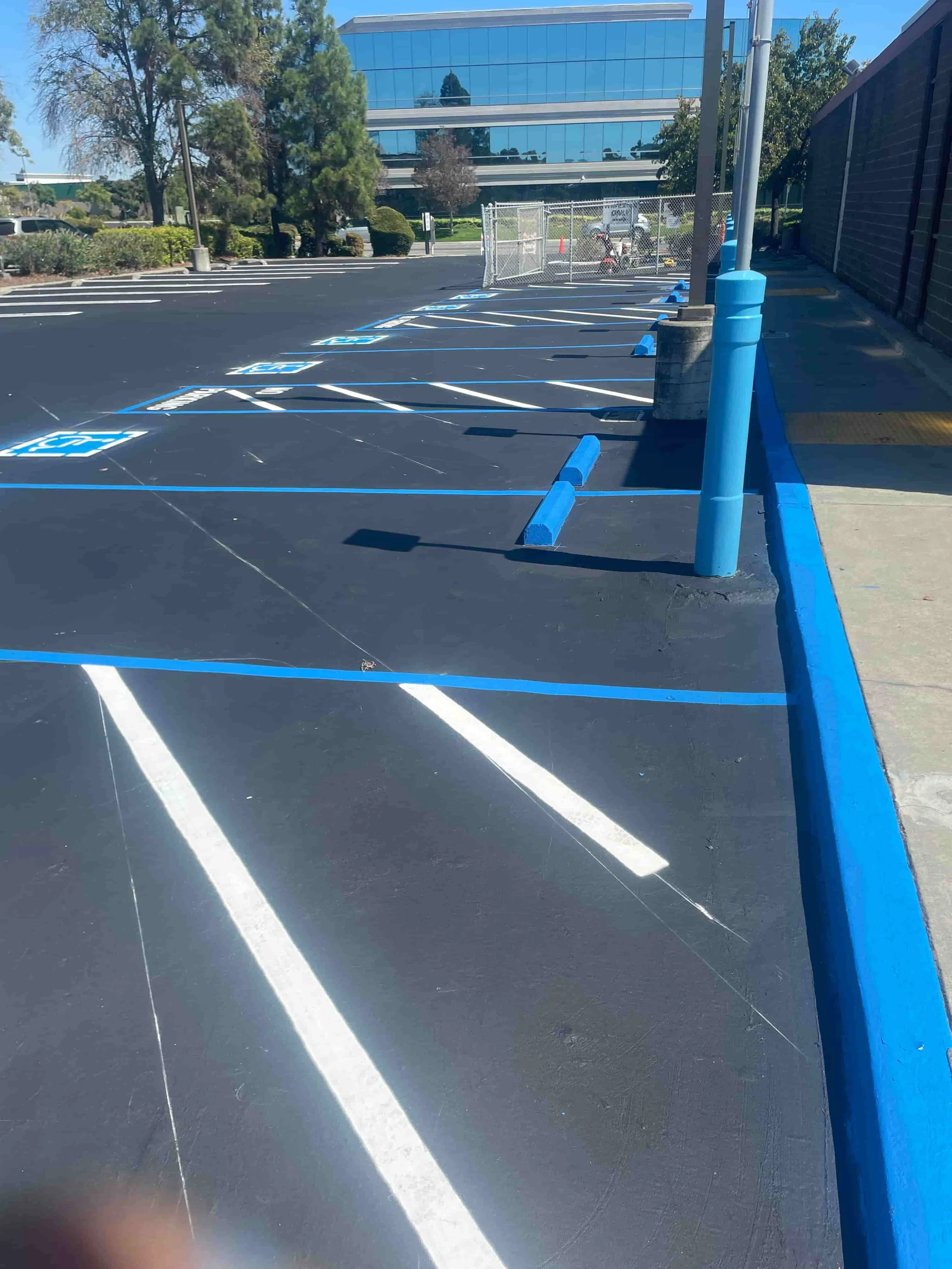 Freshly painted, empty parking lot with blue lines marking accessible spaces and a reflective building in the background.