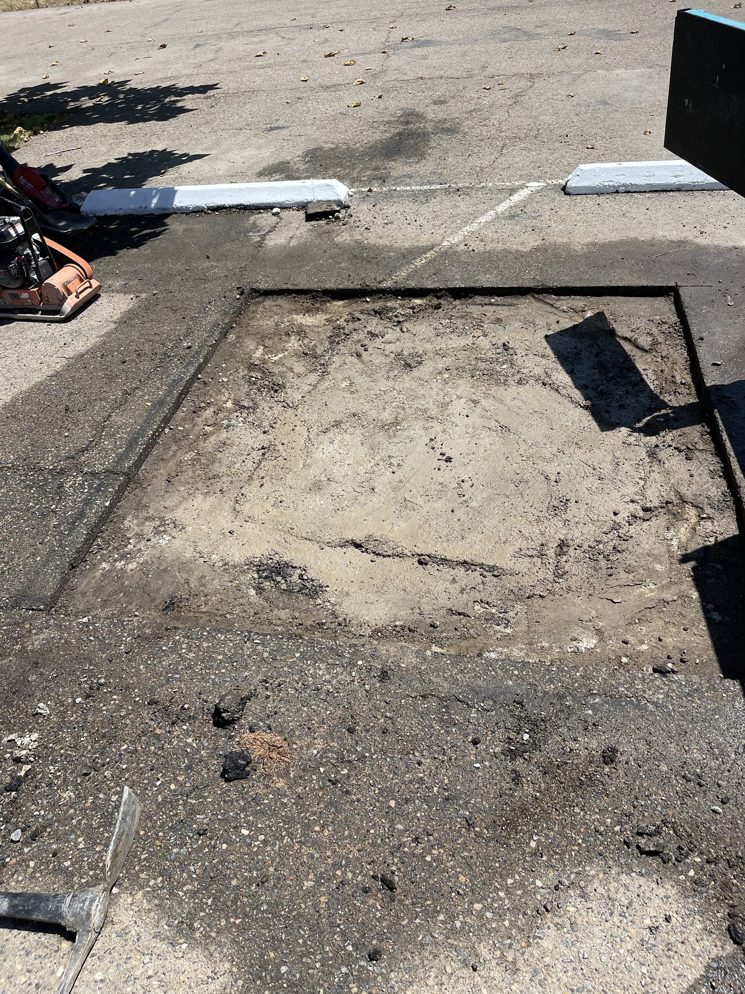 A parking lot with a section damaged asphalt cut and removed in order to do an asphalt patch