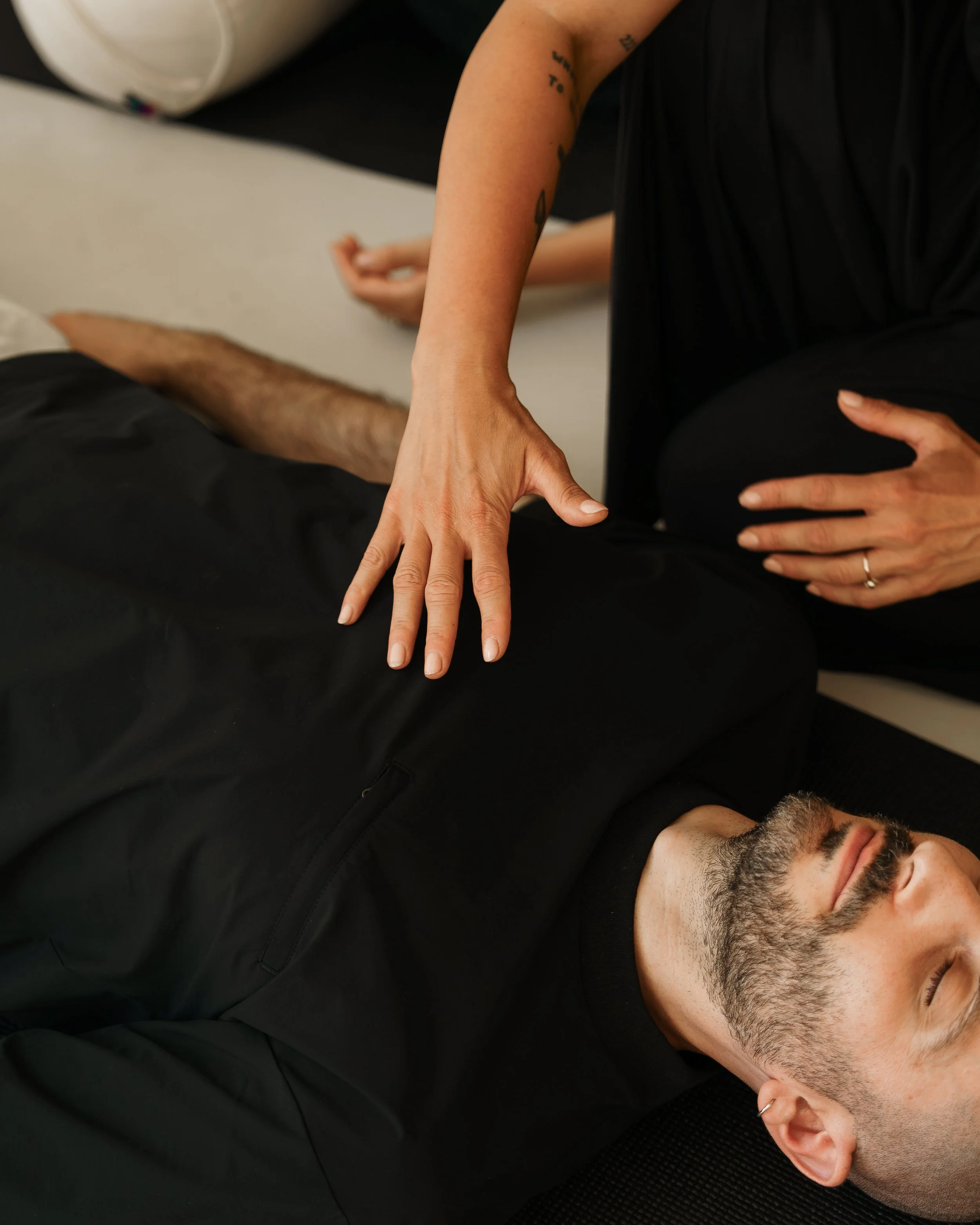Man laying down to breath, breathwork facilitator assisting.