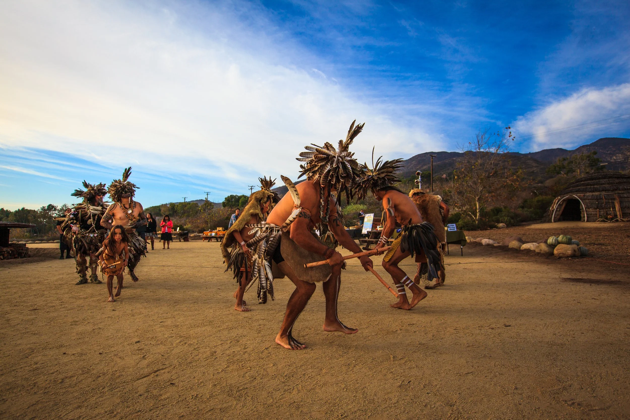 Chumash men dressed in traditional regalia dance in a circle at Wishtoyo Village.